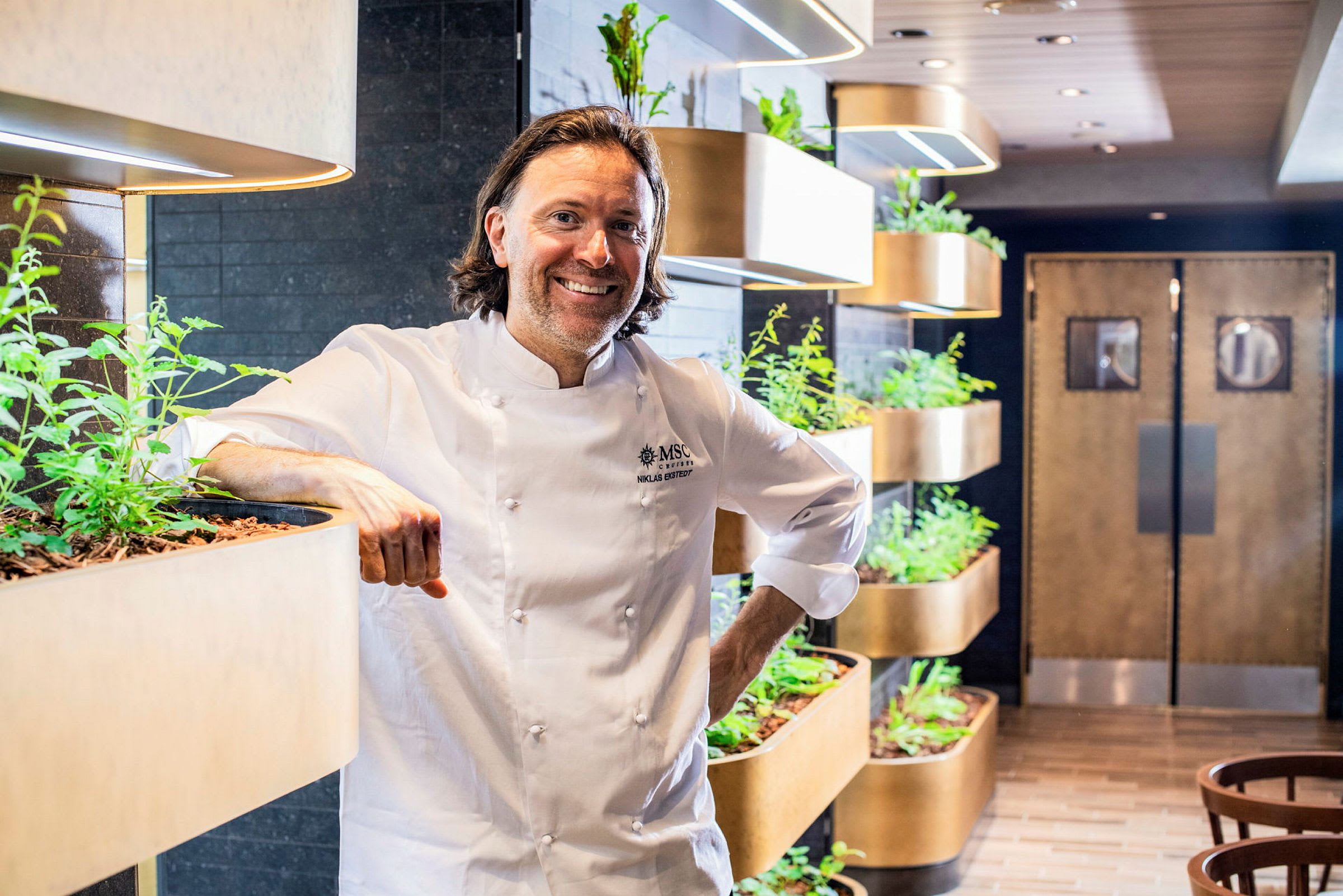 Kocken står bredvid växtinstallationer i en restaurangmiljö. (AI-genererad text)