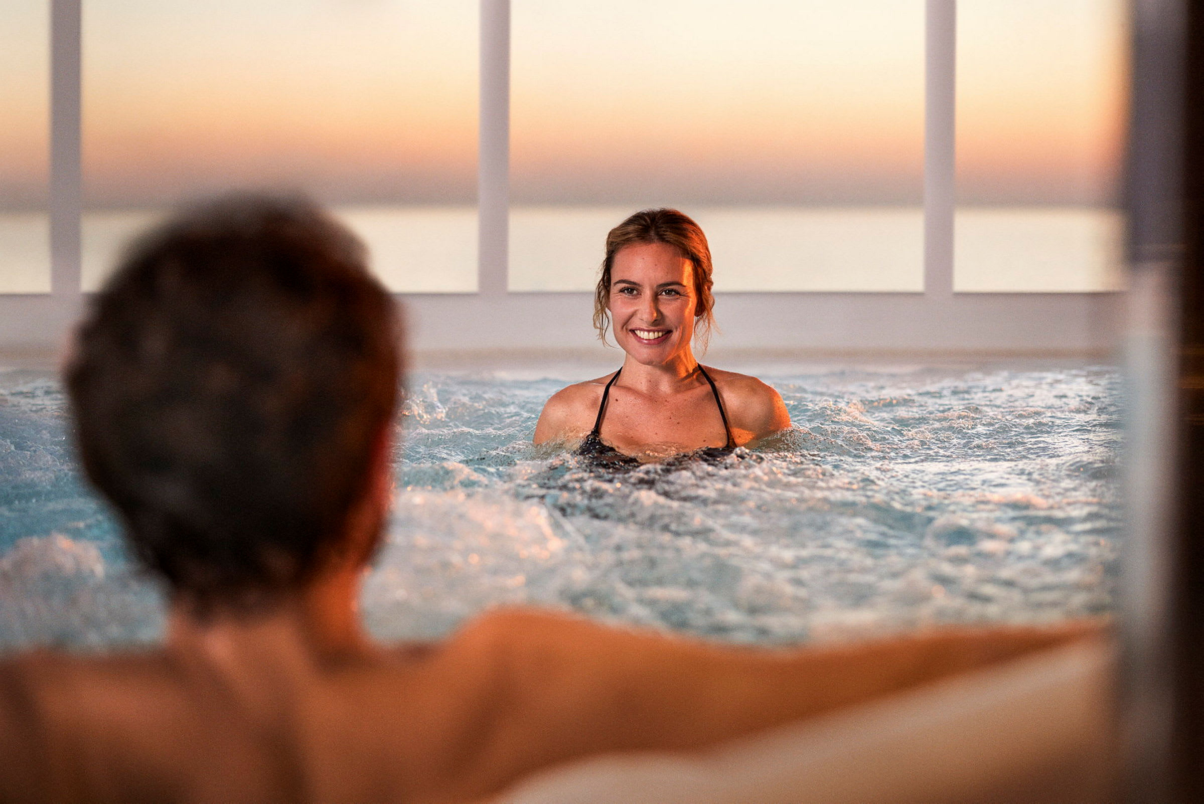 Personer njuter av en jacuzzi med en solnedgång i bakgrunden. (AI-genererad text)