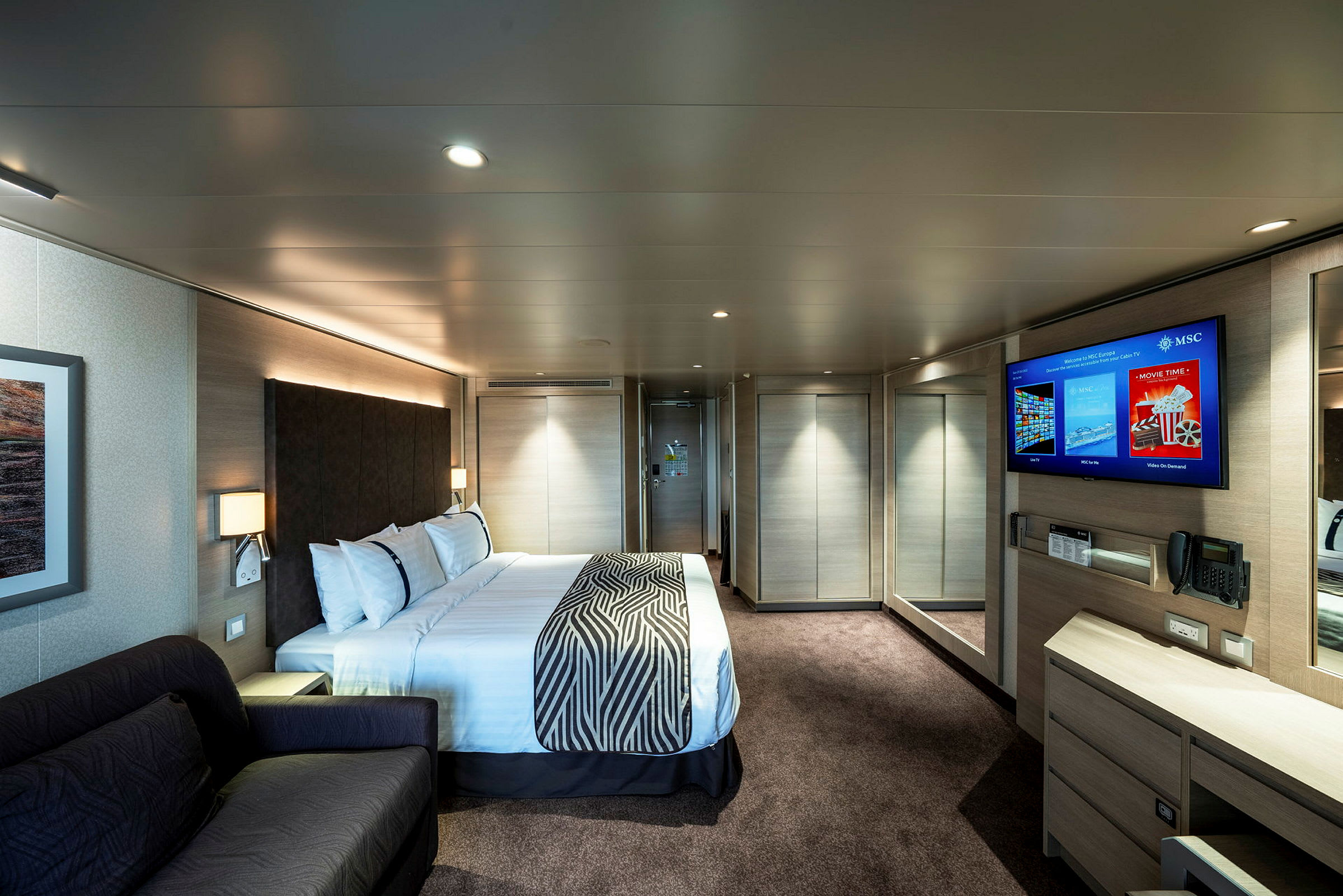 Ett hotellrum med dubbelsäng, en soffa, en TV på väggen och speglar. (AI-genererad text)