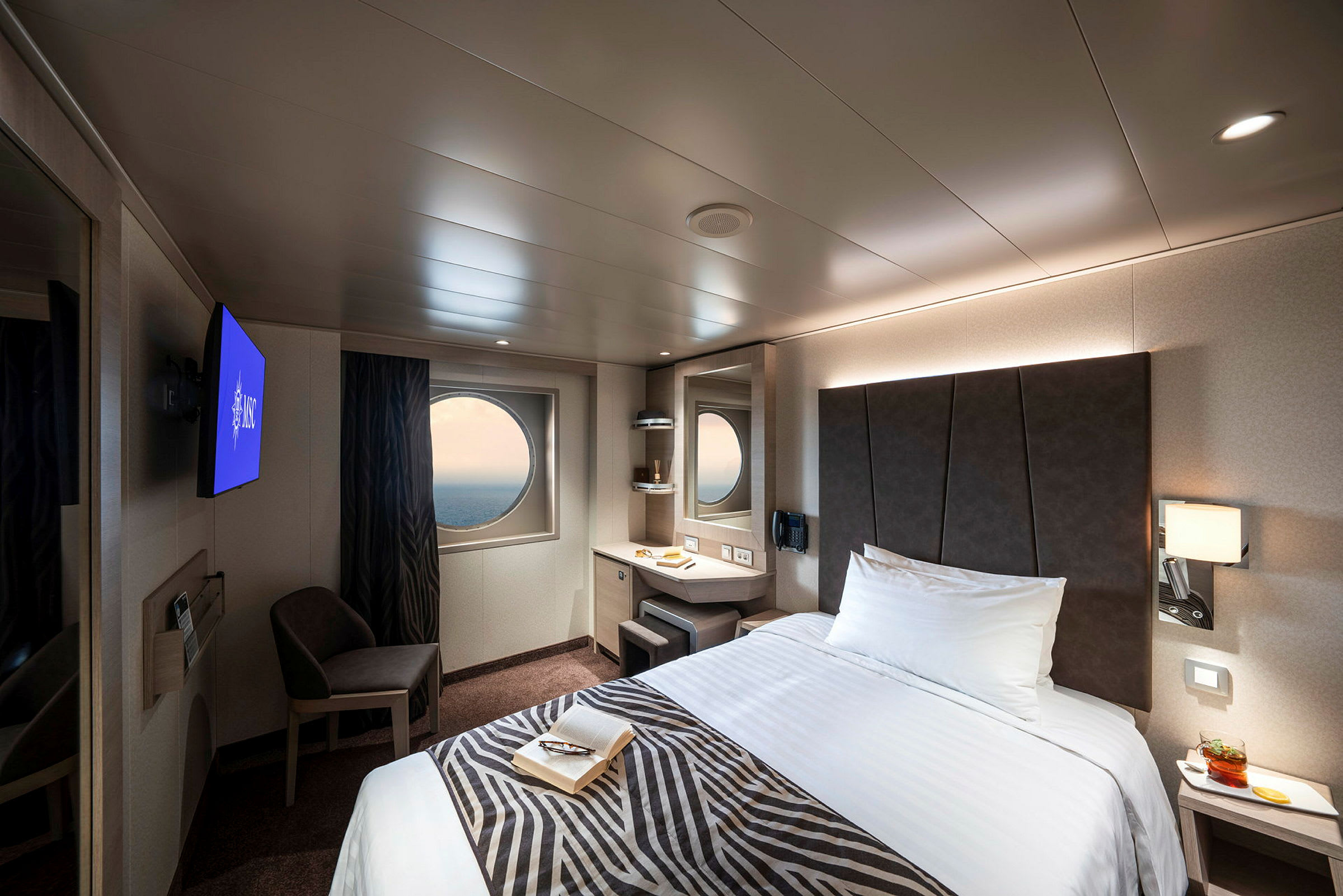 En modern hotellrumsinredning med en säng, ett runt fönster och en tv. (AI-genererad text)