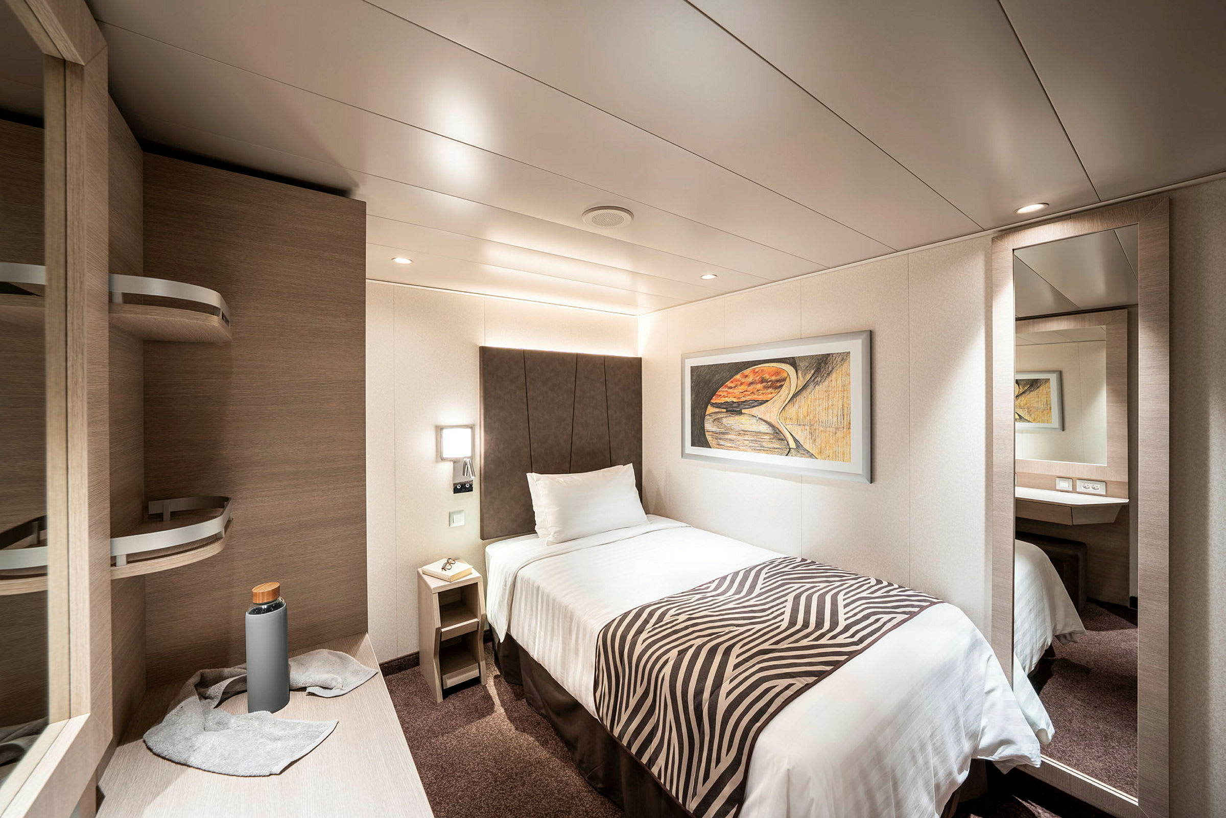 Ett hotellrum med en enkelsäng, väggkonst, och en spegel. (AI-genererad text)
