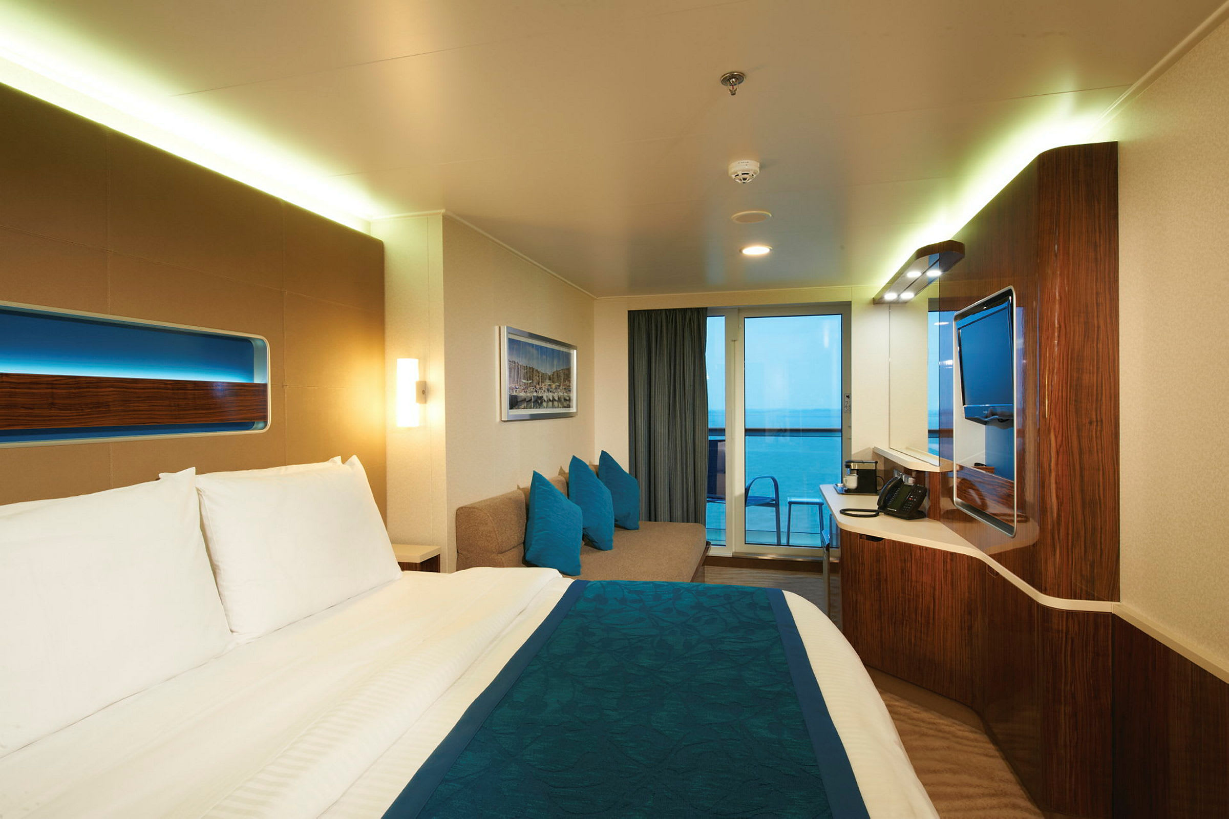 Ett hotellrum med en dubbelsäng, en soffa och en dörr som leder till en balkong med havsutsikt. (AI-genererad text)