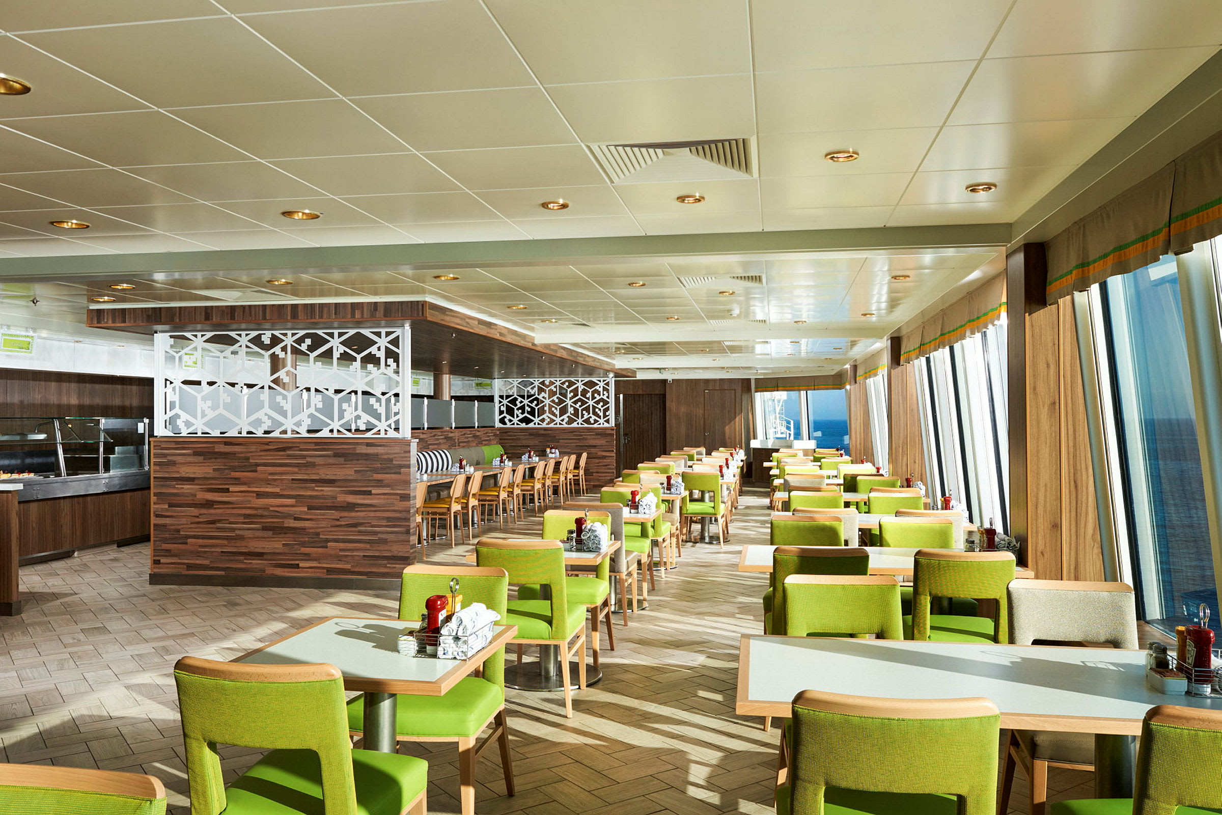 En restaurang med grönklädda stolar och bord placerade i rader, med fönster som visar havet utanför. (AI-genererad text)