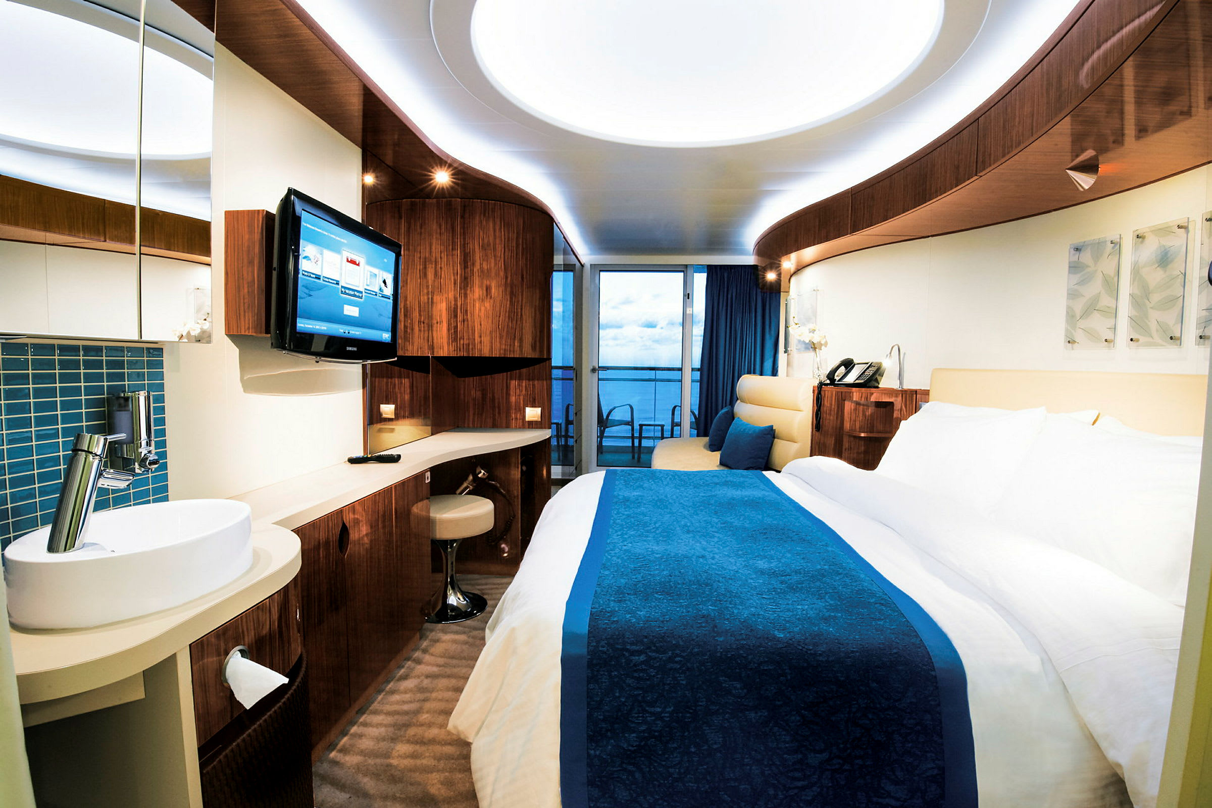 Ett hotellrum med modern inredning, en säng med blå överkast, ett skrivbord, och en balkong med utsikt. (AI-genererad text)