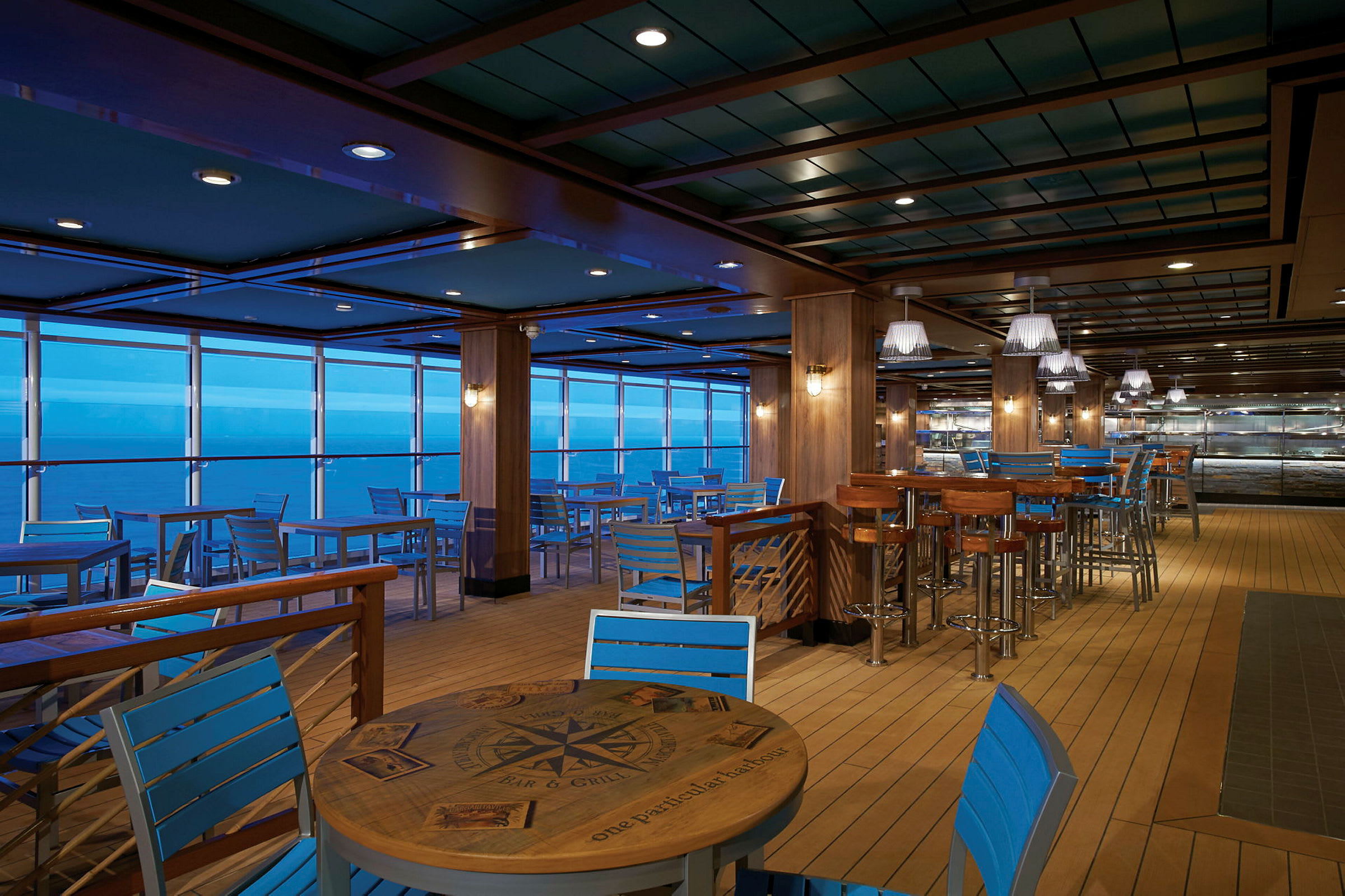 Restaurang med blå stolar och träbord, havsutsikt i bakgrunden. (AI-genererad text)