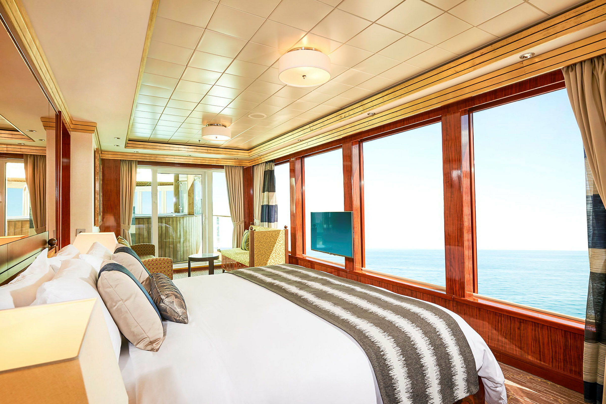 Ett rymligt hotellrum med stor säng, sittgrupp och panoramautsikt över havet genom stora fönster. (AI-genererad text)
