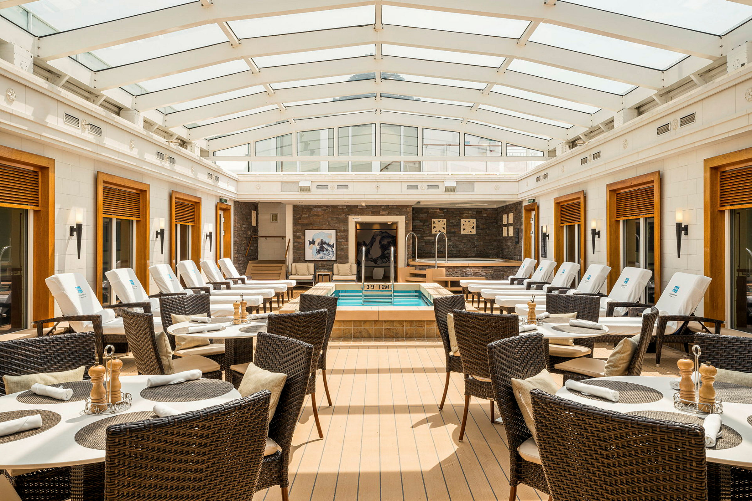 Interiörbild som visar en spa-avdelning med sittplatser och solstolar, samt en liten pool. (AI-genererad text)