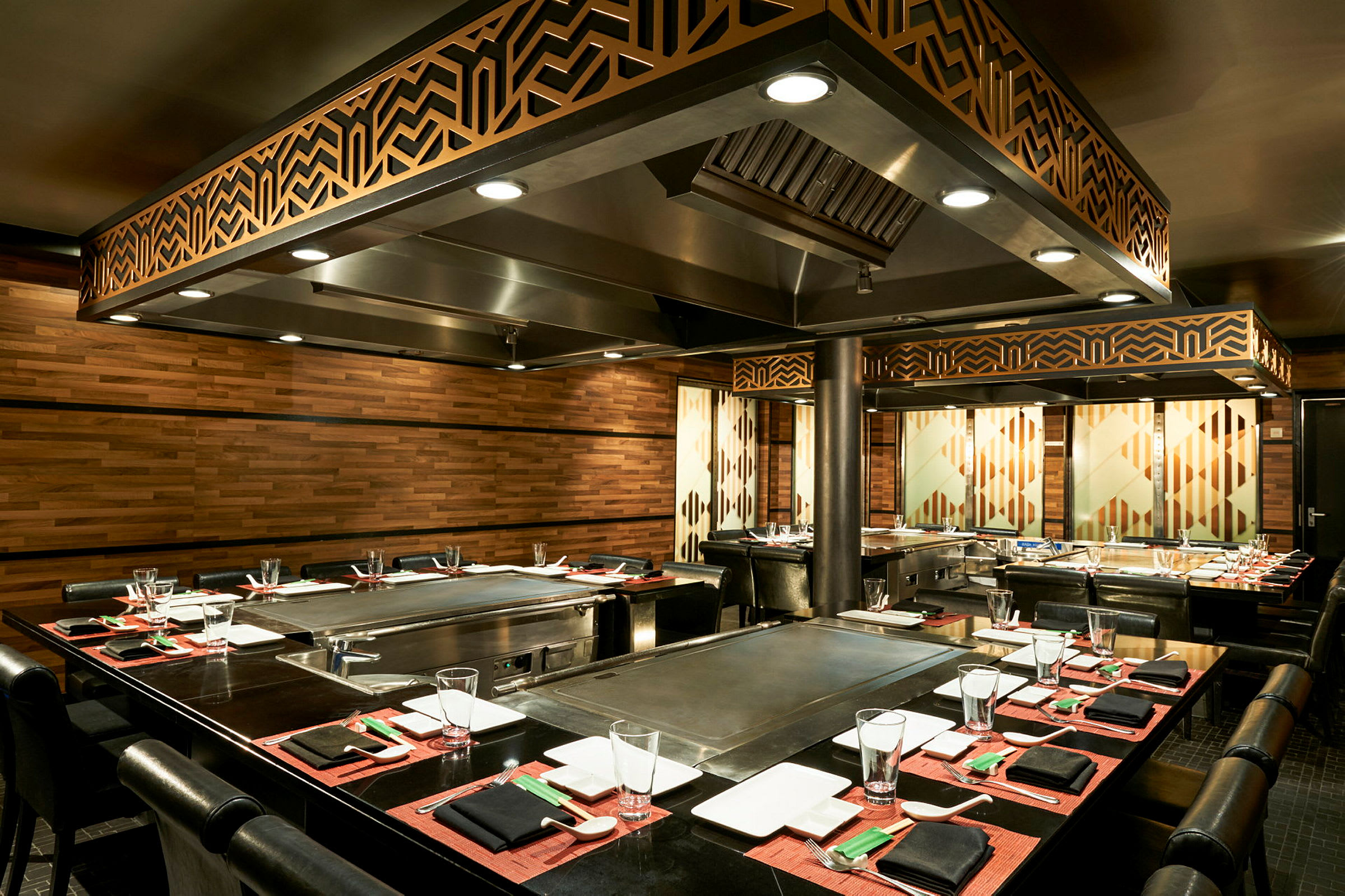 Ett teppanyaki-restaurangbord med elegant dukning, omgiven av träpaneler och belysning. (AI-genererad text)
