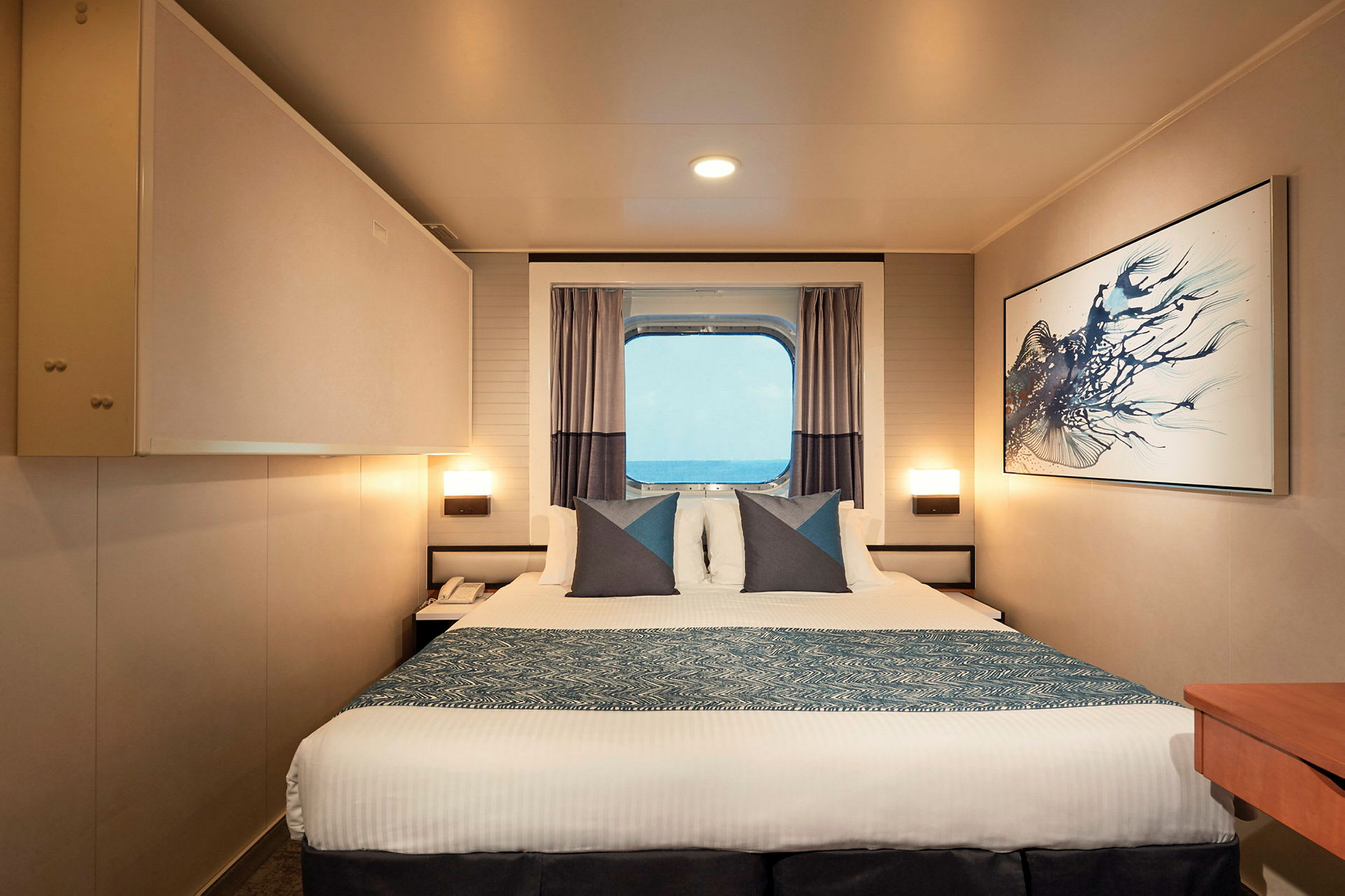 Ett hotellrum med en säng, konst på väggen och ett fönster med utsikt över havet. (AI-genererad text)