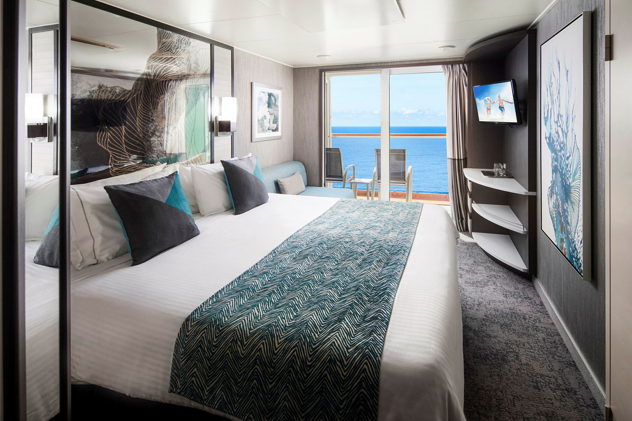Hotellrum med dubbelsäng, kuddar och utsikt mot havet genom glasdörrar. (AI-genererad text)
