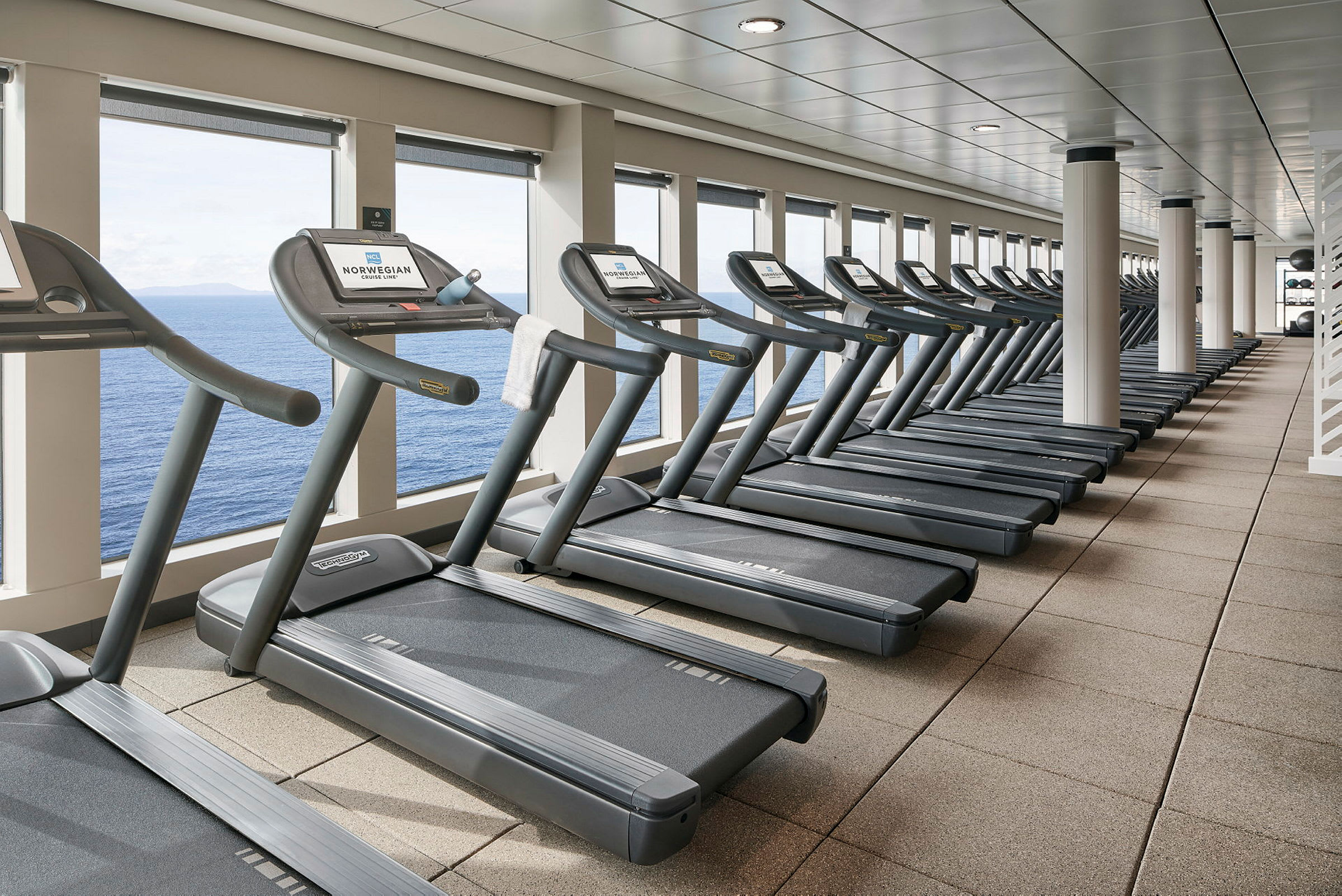 En rad av löpband vid ett gym med utsikt över havet. (AI-genererad text)