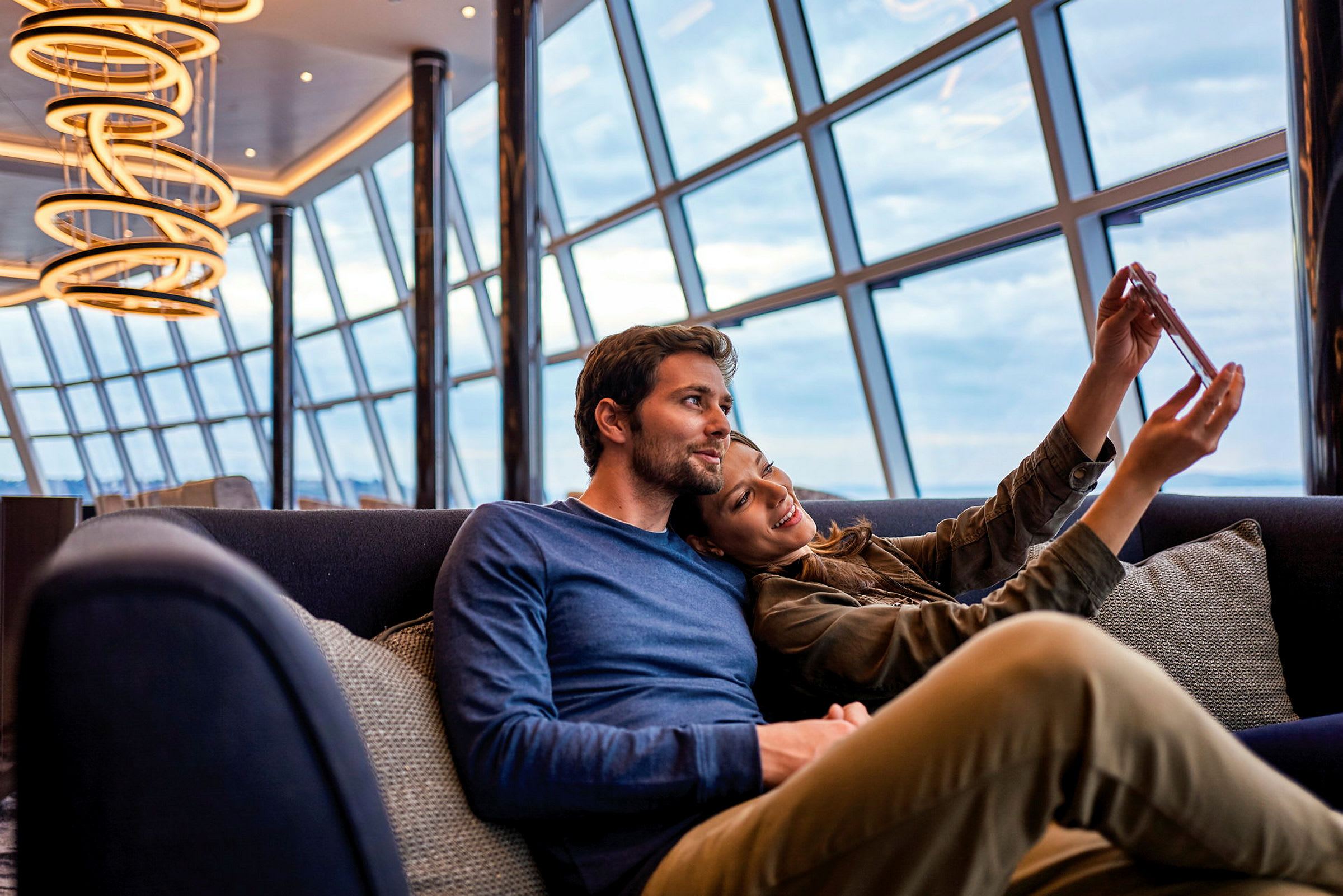 En modern lounge med stora fönster och upphängda ljuskronor. (AI-genererad text)