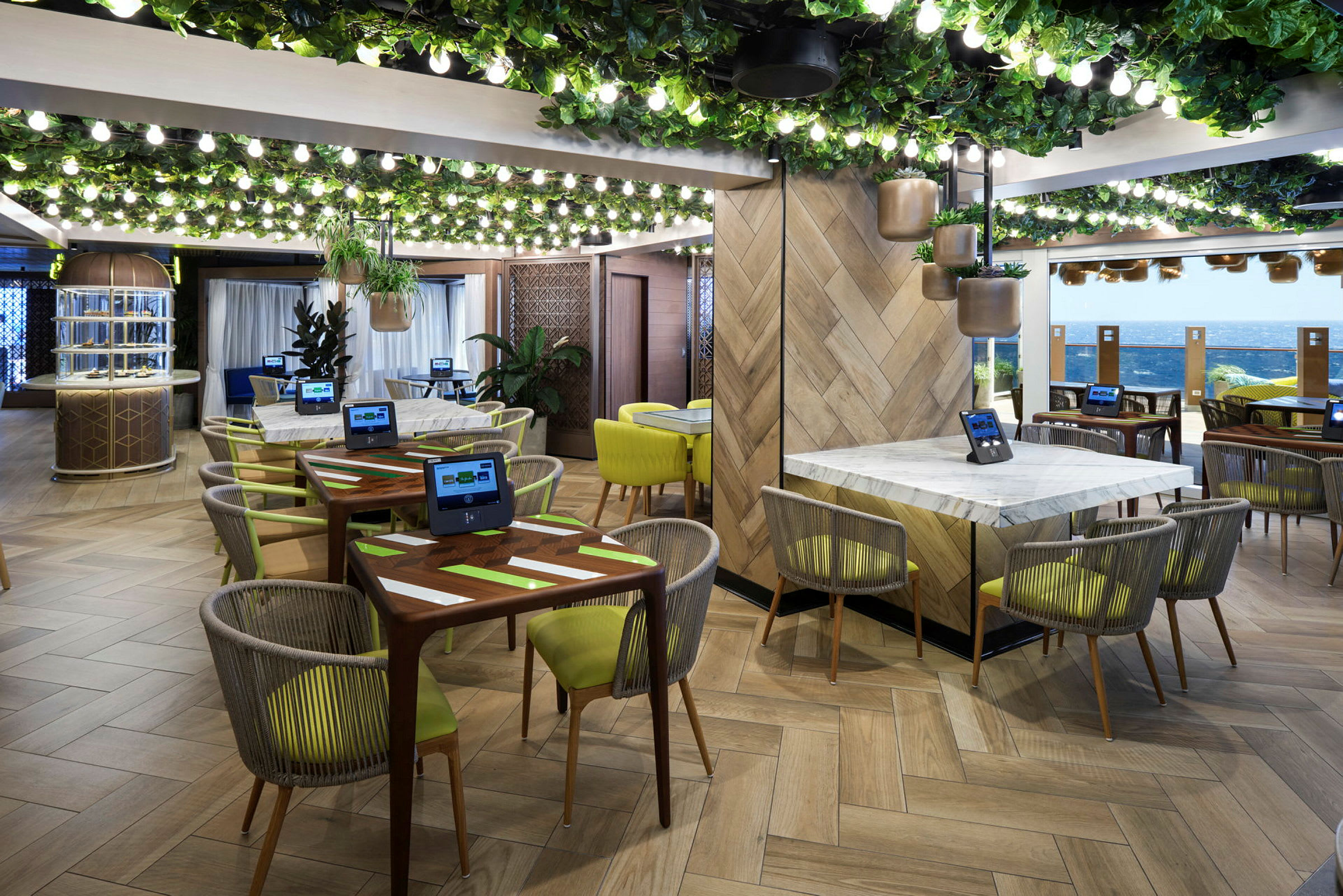 Restaurang med modern inredning, gröna planteringar och bord med skärmar. (AI-genererad text)