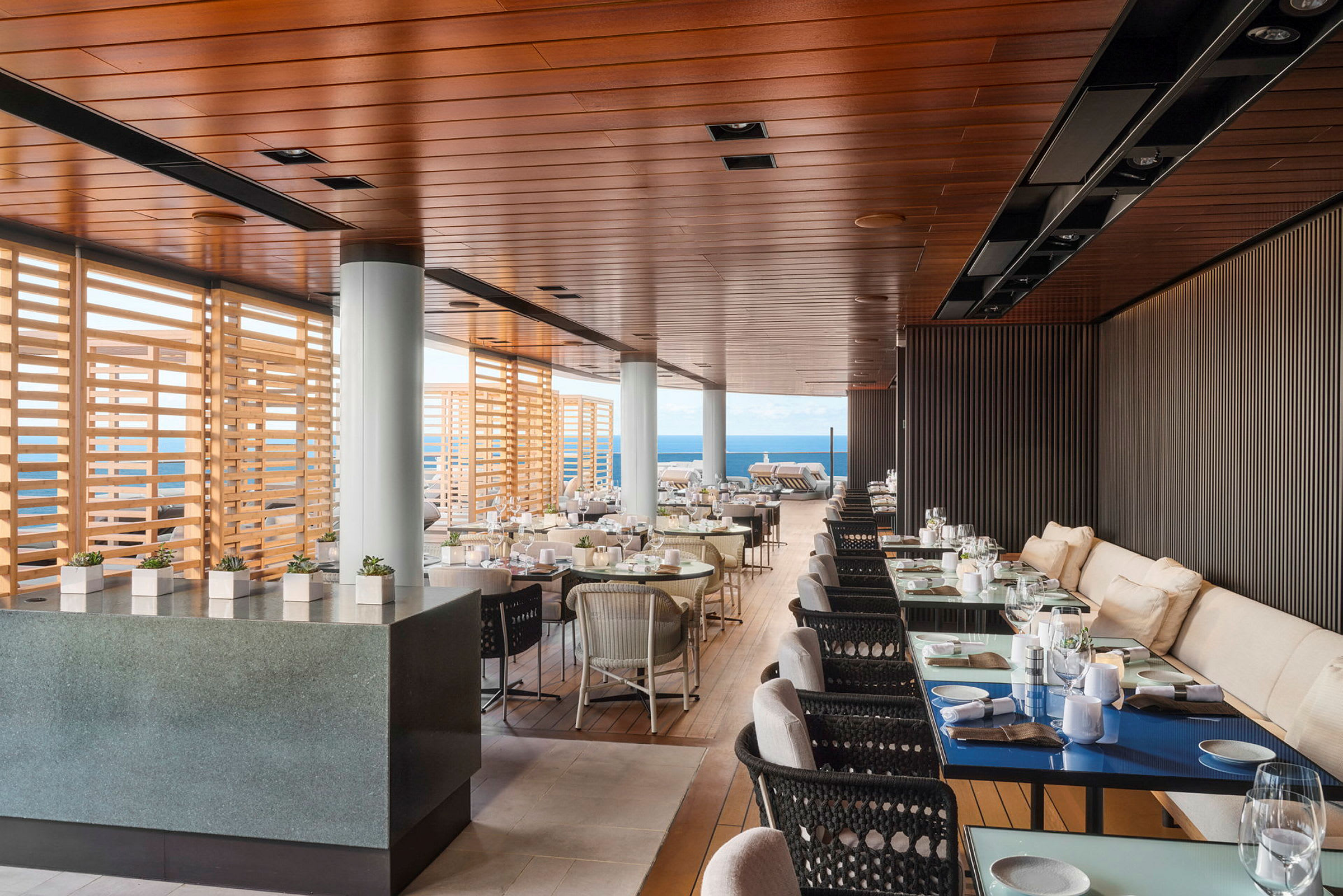 En elegant restaurang med havsutsikt, inomhus- och utomhusområden, med trädetaljer och modernt inrett. (AI-genererad text)