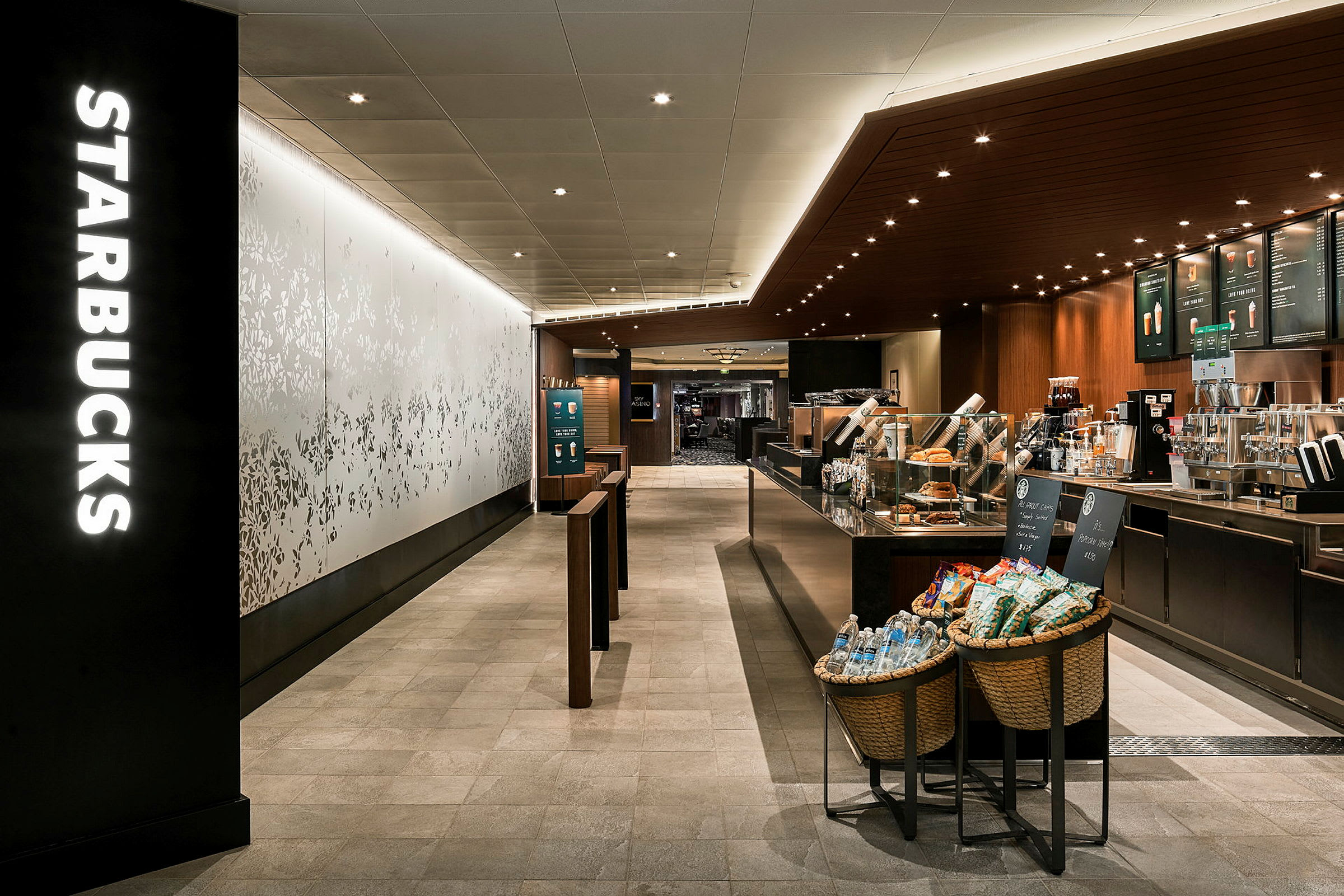 En interiörbild av ett Starbucks-kafé med kaffemaskiner, menybrädor och varor vid entrén. (AI-genererad text)