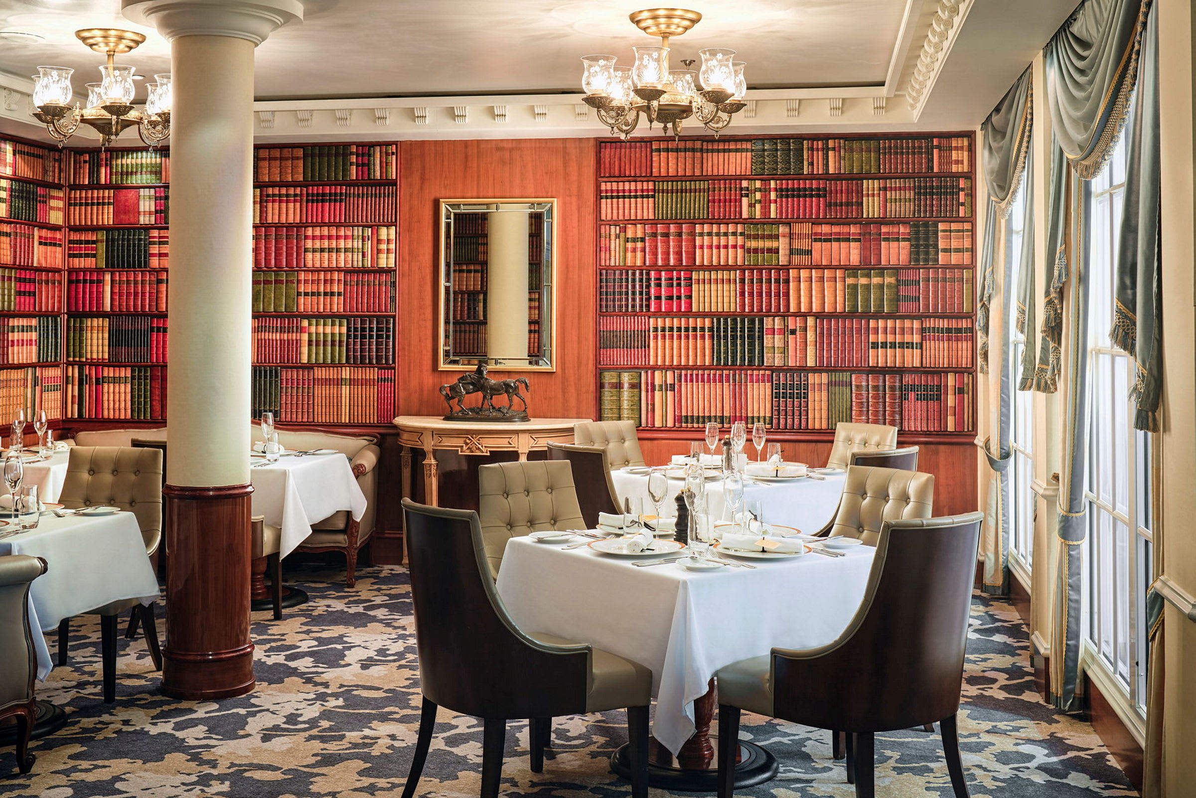 En elegant restaurang med bord täckta av vita dukar, omringad av bokhyllor samt stort fönster och rika gardiner. (AI-genererad text)