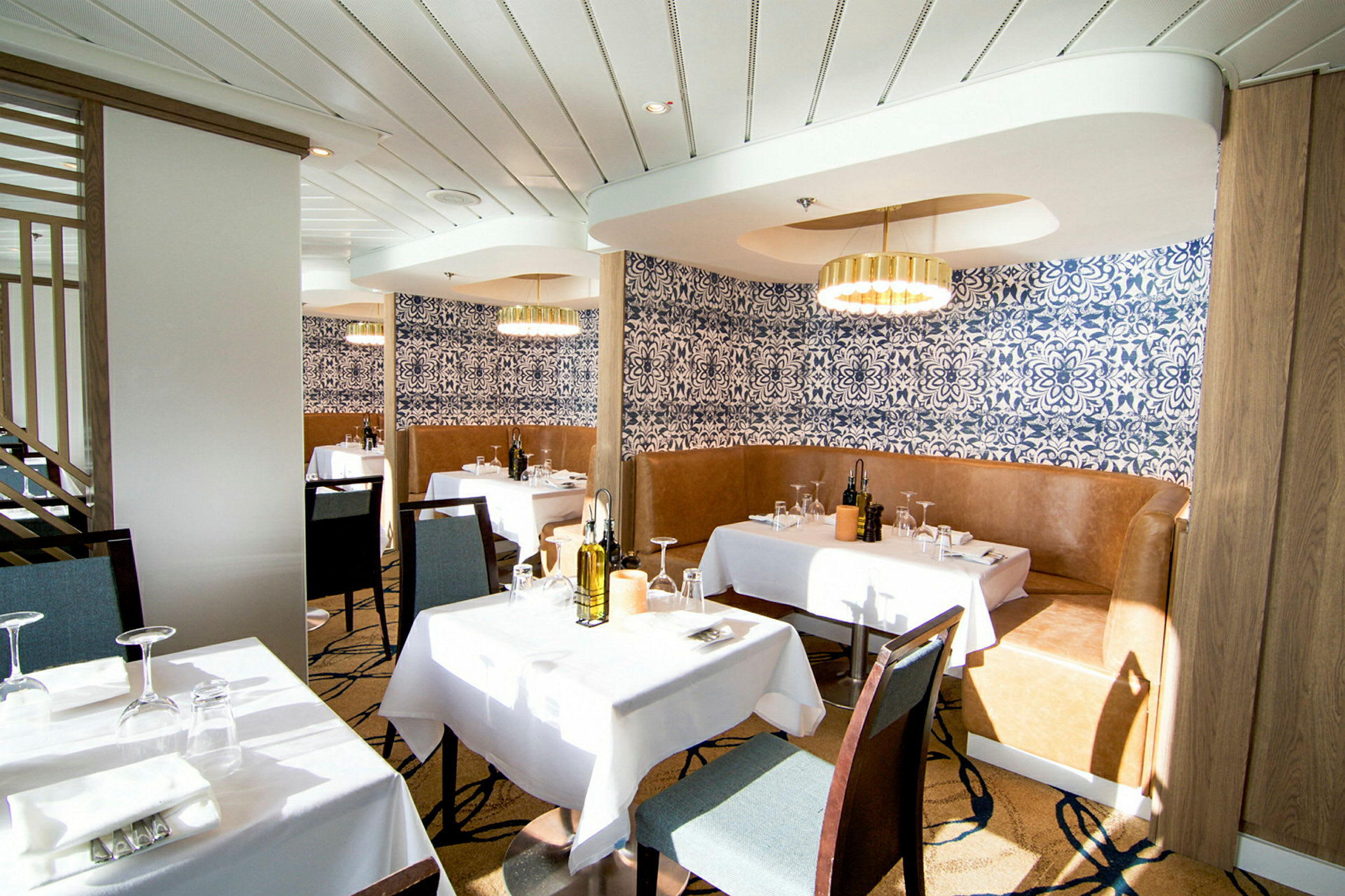 En elegant restaurang med vita dukar, blå mönstrade tapeter och moderna ljuskronor. (AI-genererad text)