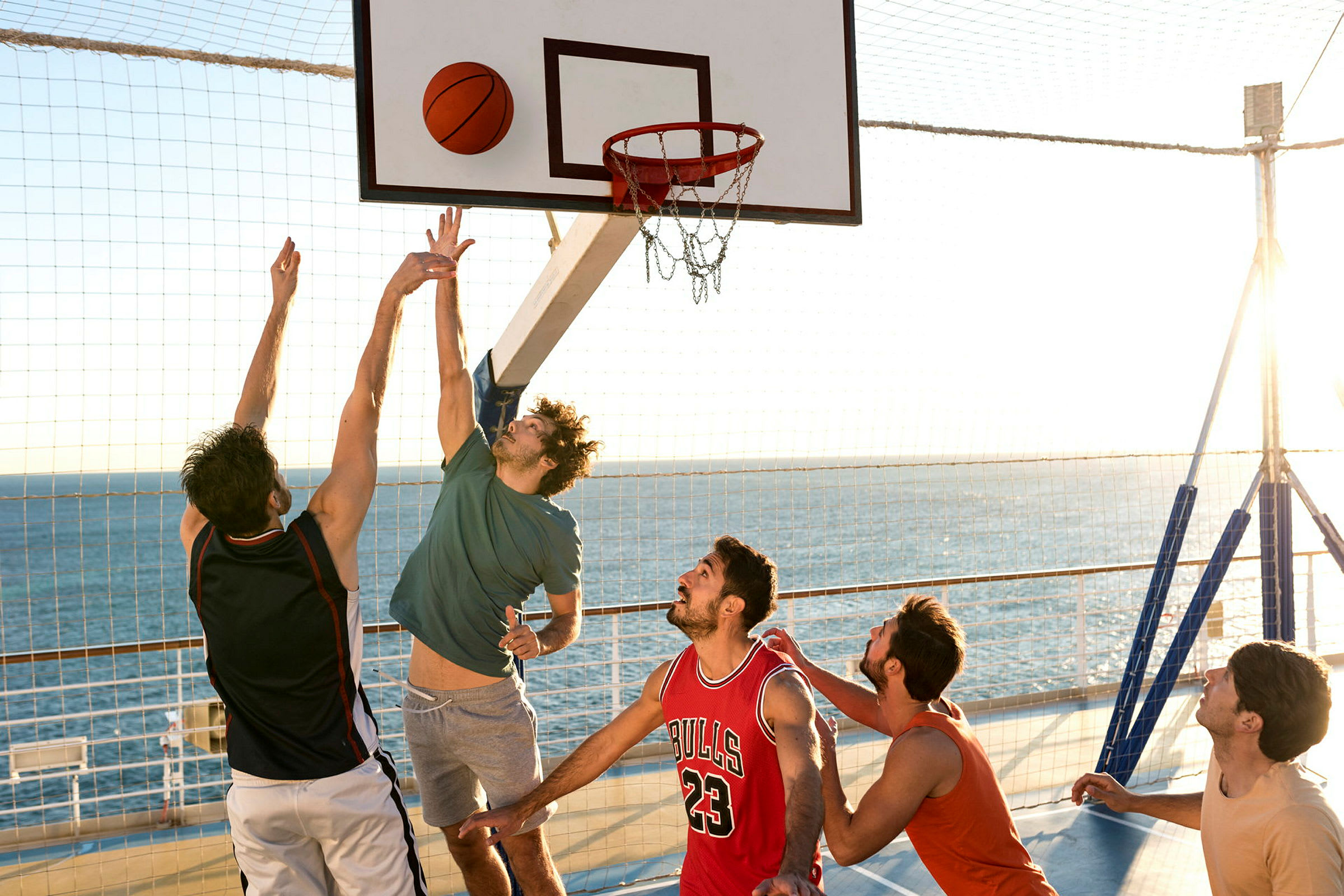 Personer spelar basket nära havet under solnedgången. (AI-genererad text)