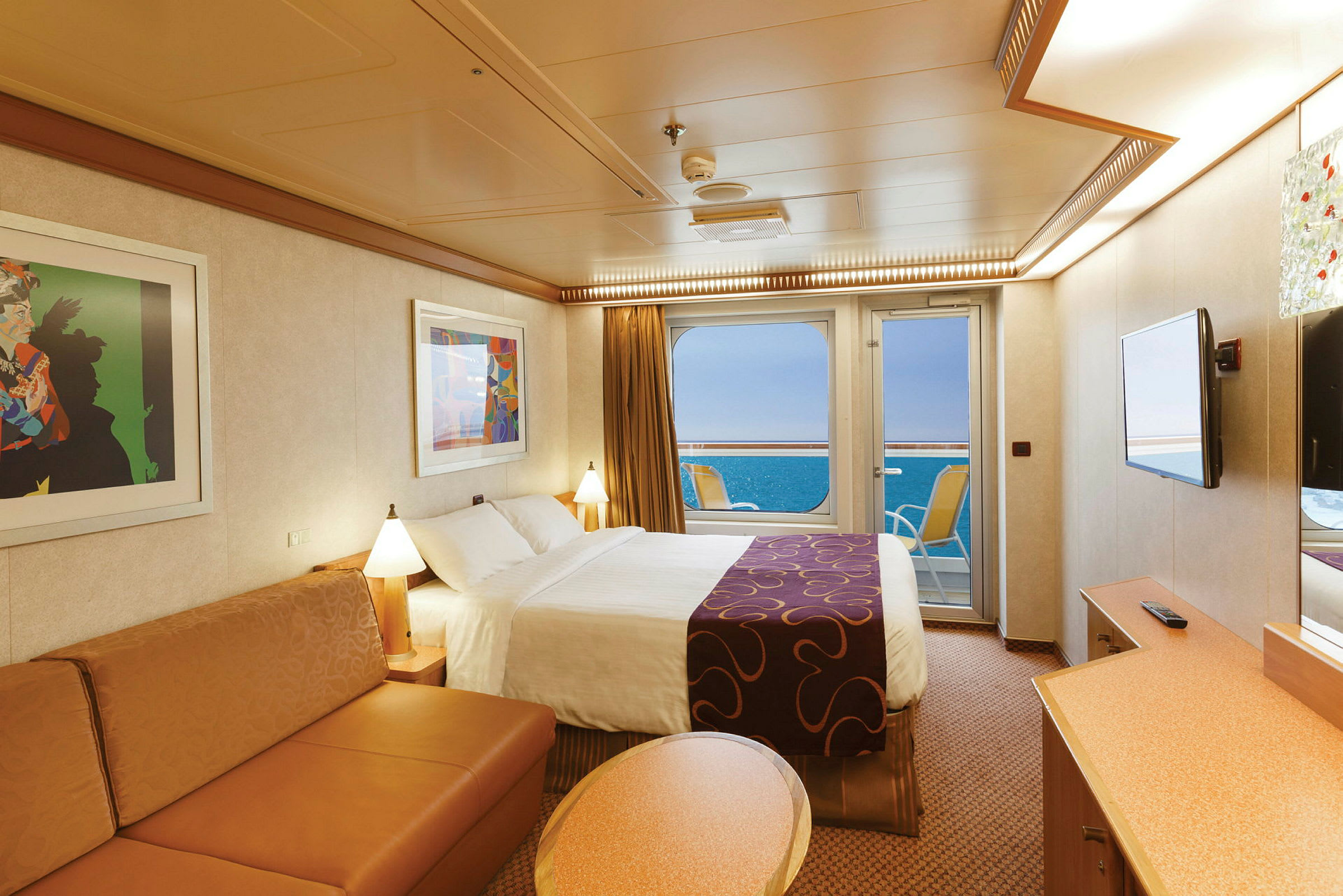 Ett hotellrum med säng, soffa, två tavlor och en glasdörr som vetter mot havet. (AI-genererad text)