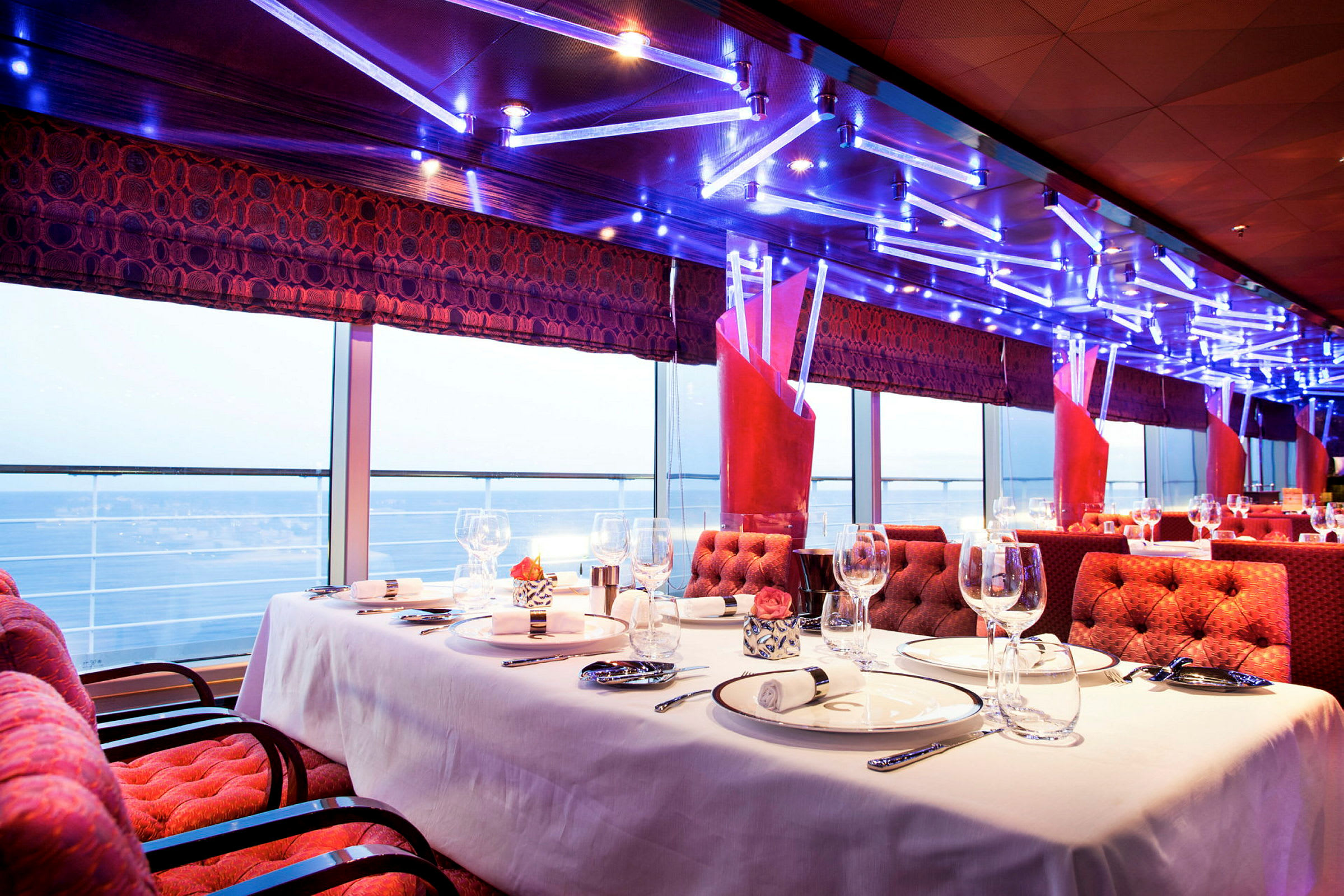 Elegant restauranginteriör med dukat bord och havsutsikt genom panoramafönster. (AI-genererad text)