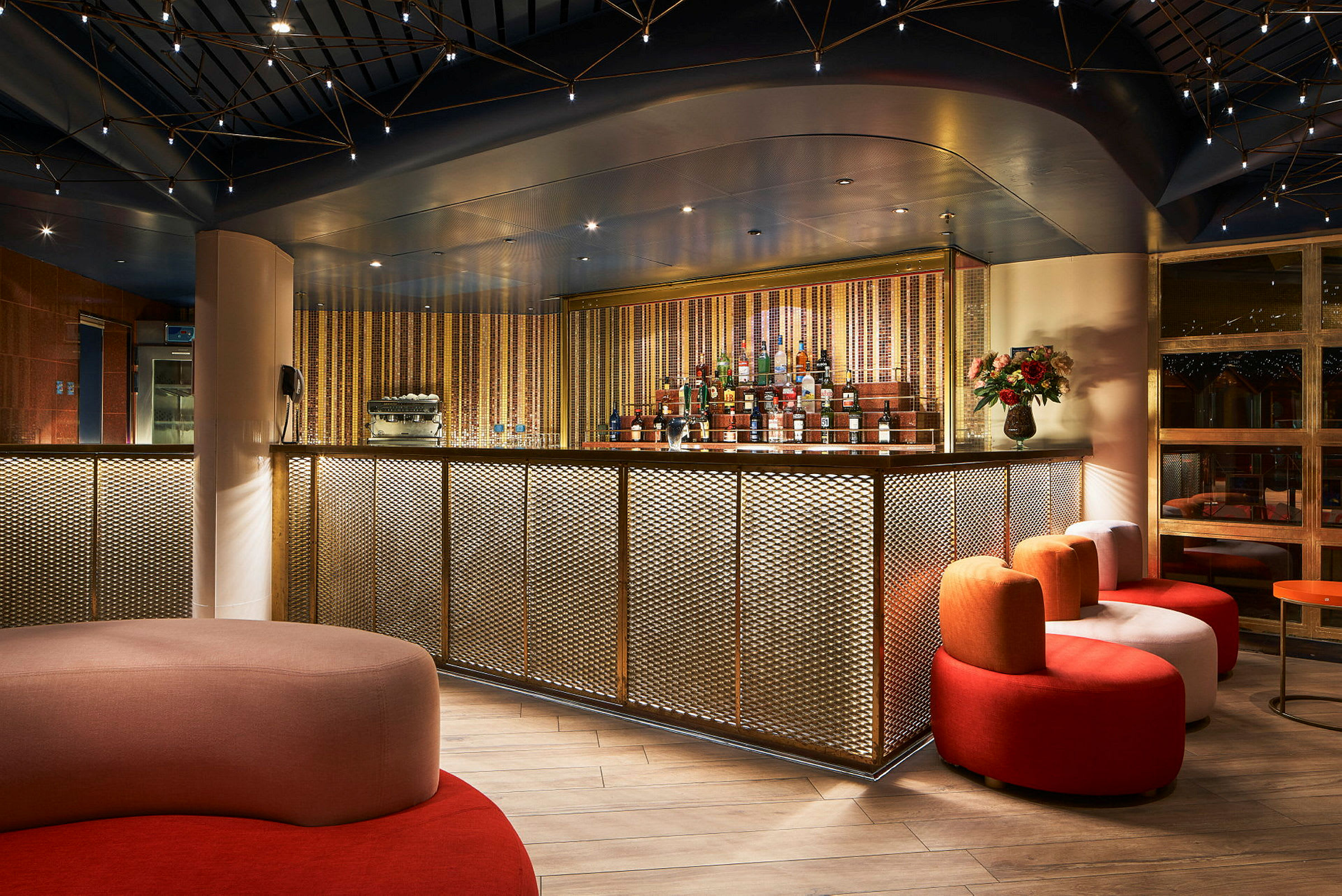 En elegant bar med guldmönstrad front, sittmöbler i olika färger och en varm belysning. (AI-genererad text)