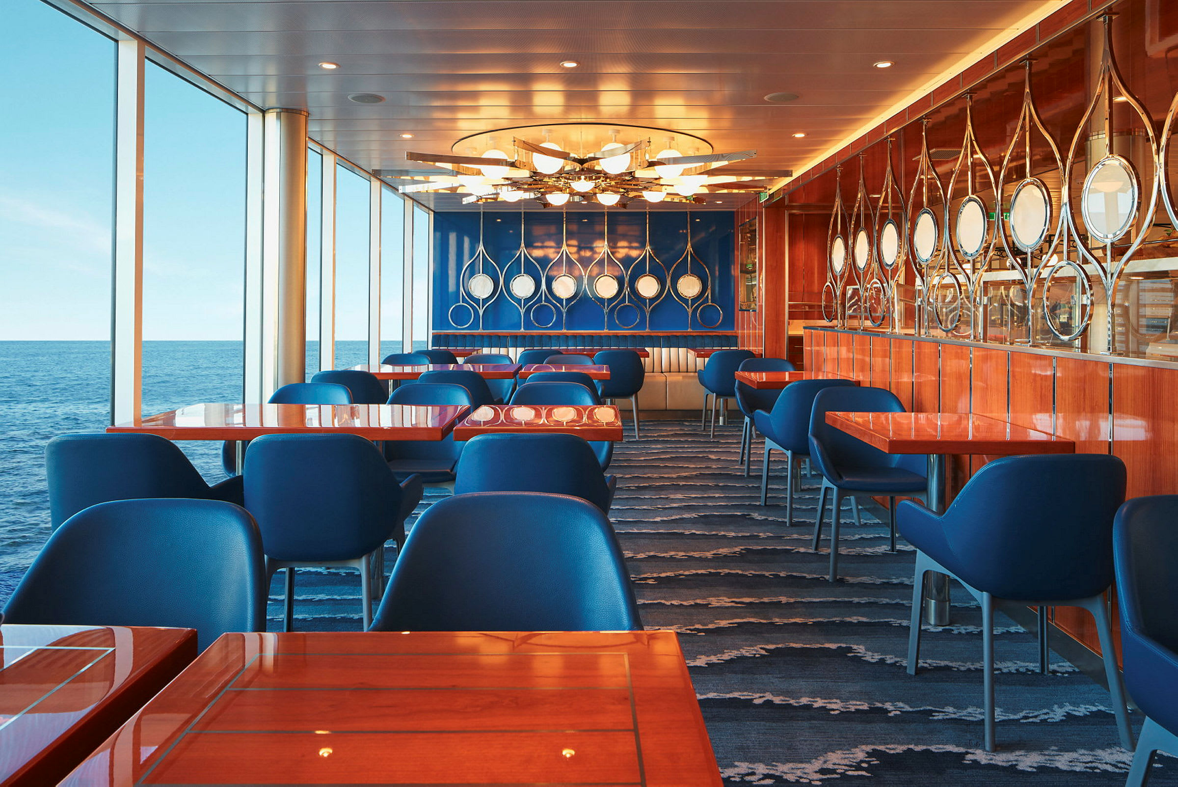 Restaurang med blå stolar, bord med träyta och panoramafönster mot havet. (AI-genererad text)