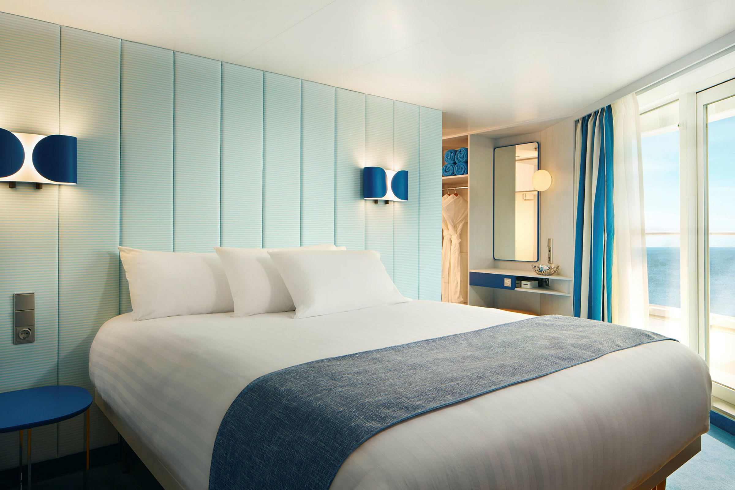 Ett hotellrum med en dubbelsäng, ljus inredning och balkongdörrar som vetter mot havet. (AI-genererad text)