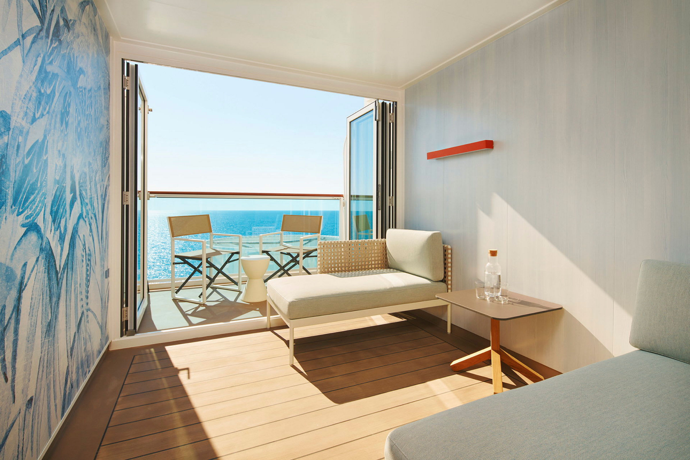 Ett modernt hotellrum med en uteplats, två stolar och bord samt utsikt över havet. (AI-genererad text)
