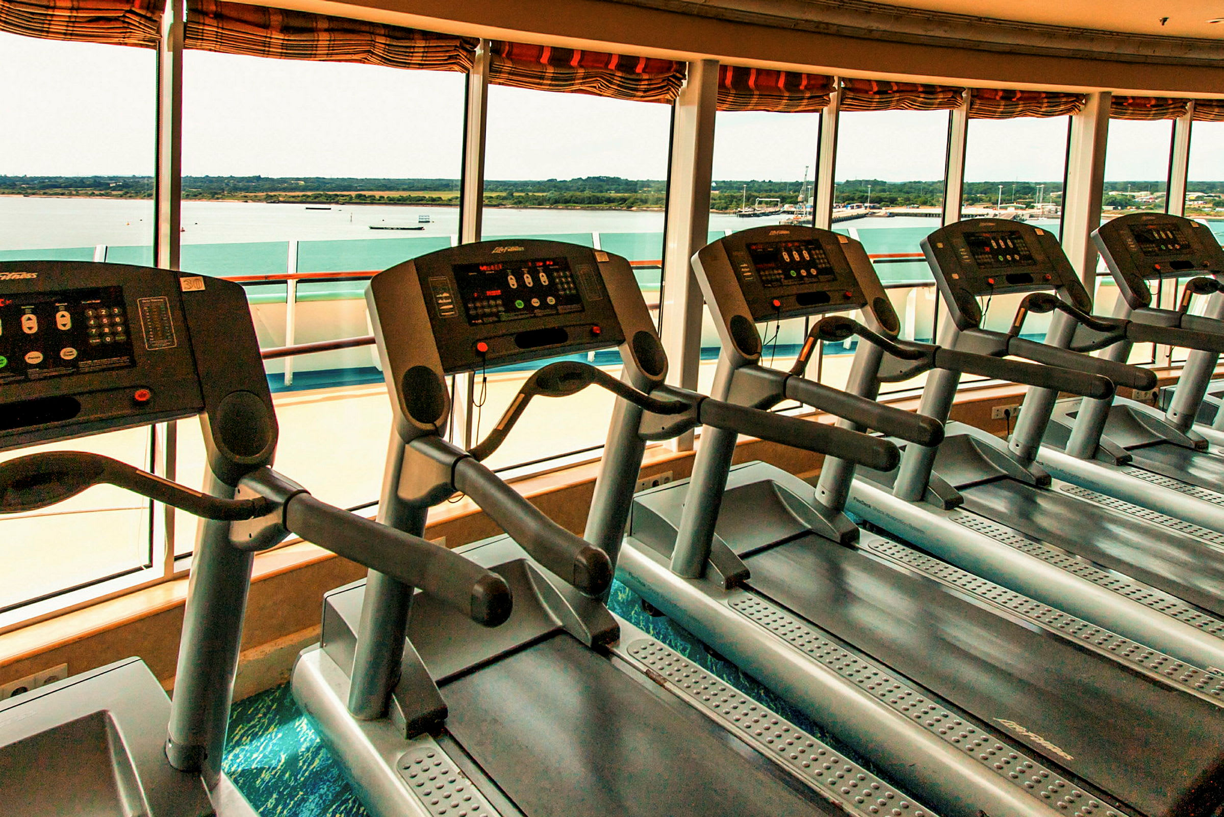 Löpband i ett gym med utsikt över vattnet genom stora fönster. (AI-genererad text)
