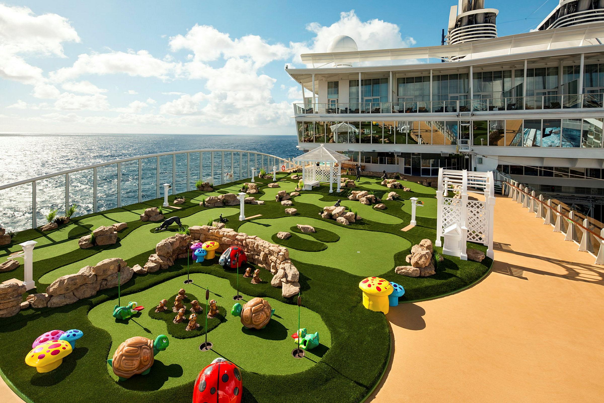 Bilden visar en minigolfbana ombord på ett kryssningsfartyg. Banan har konstgräs med stenutsmyckningar och färgglada dekorationer, samt havet i bakgrunden. (AI-genererad text)