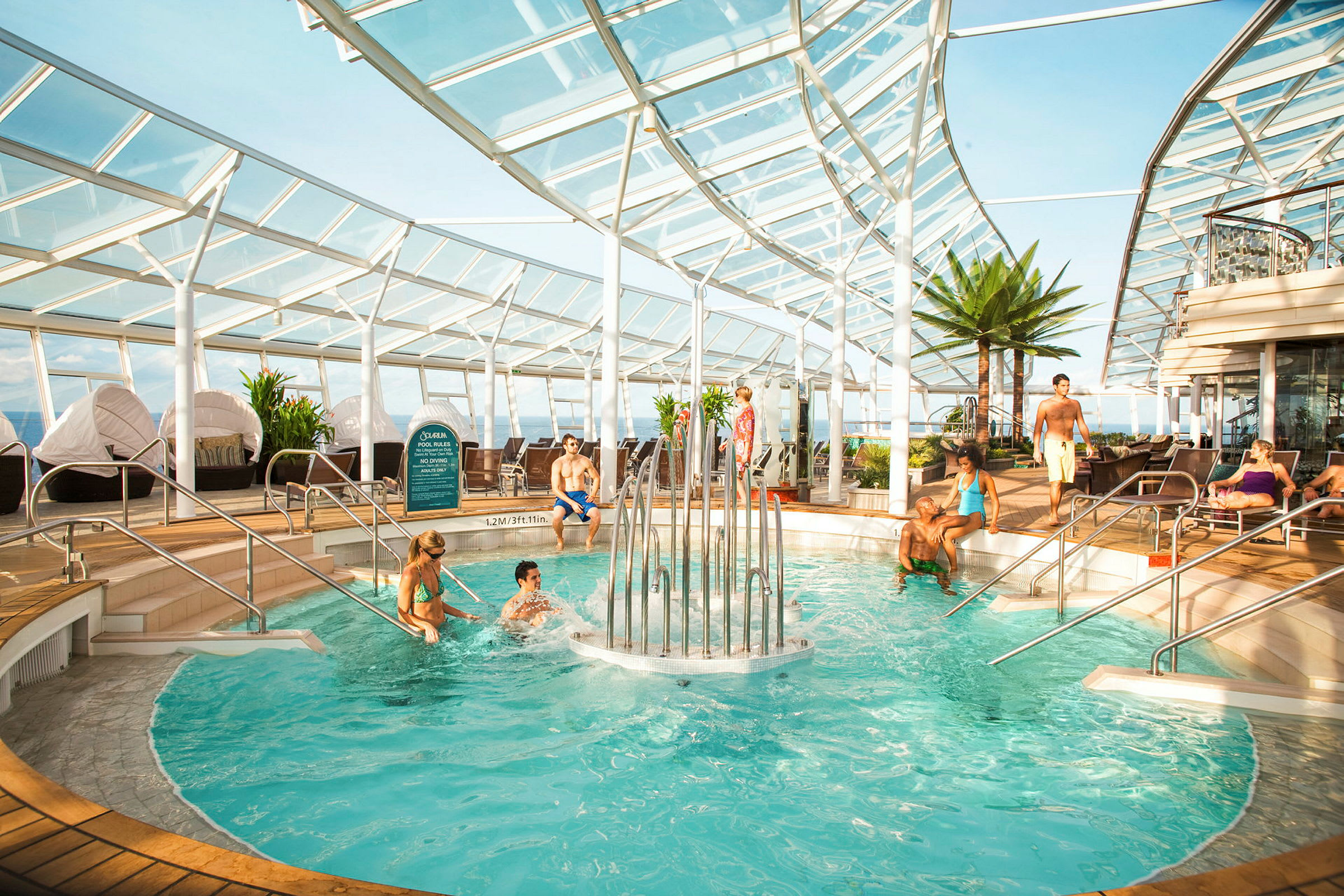 En glasinkapslad pool med människor som badar och kopplar av samt grönskande växter runtom. (AI-genererad text)