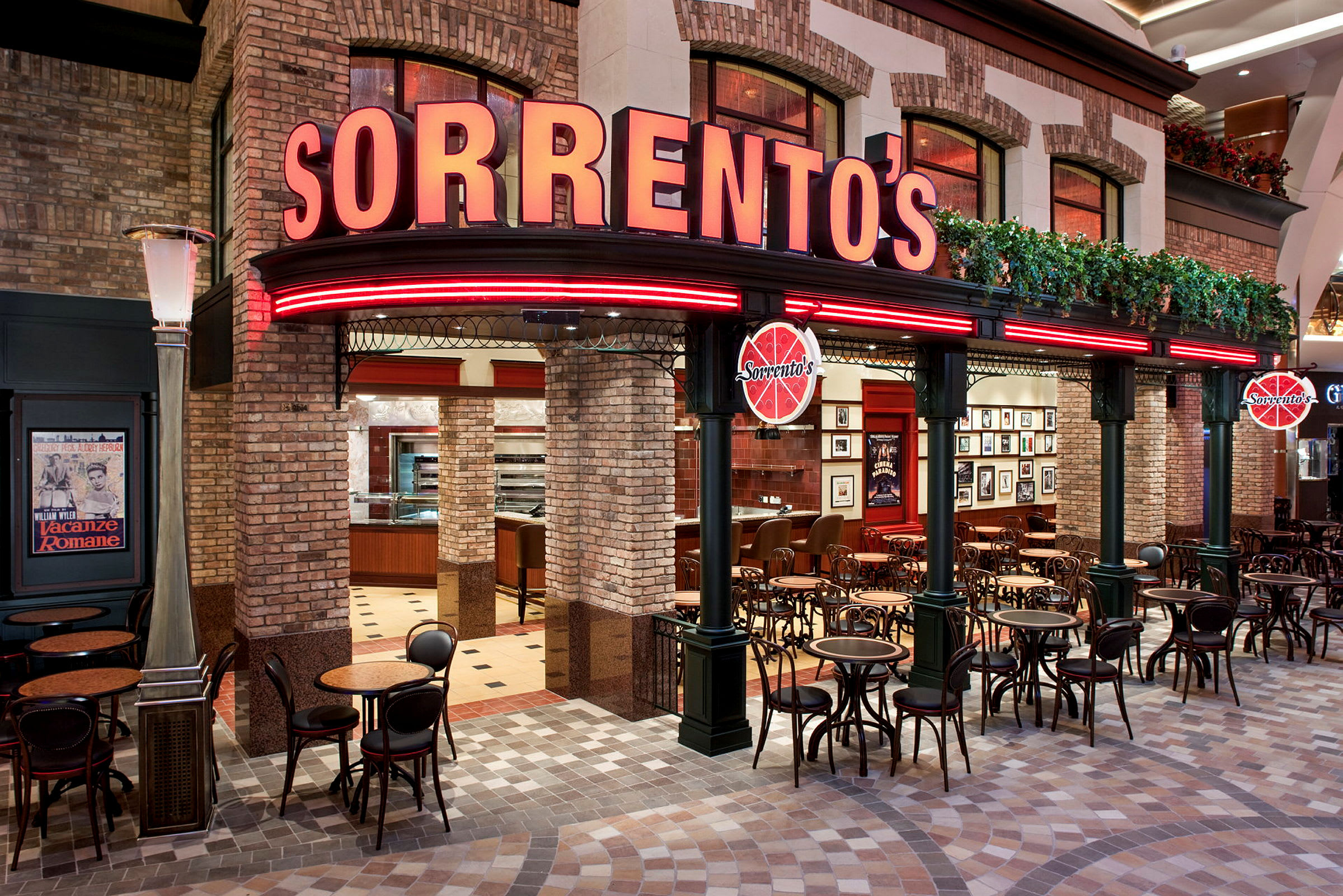Exteriör av en restaurang med namnet "Sorrento's". Byggnaden har tegelväggar och röda neonskyltar. Framför restaurangen finns små borden och stolar. (AI-genererad text)