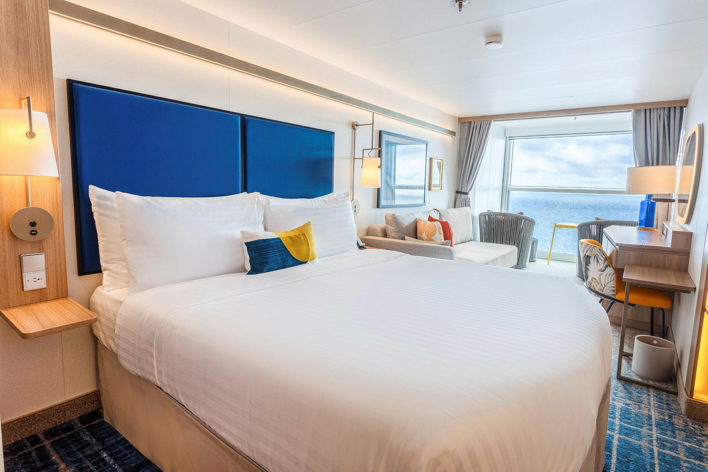 Ett ljust hotellrum med en stor säng, sittgrupp och en utsikt över havet. (AI-genererad text)
