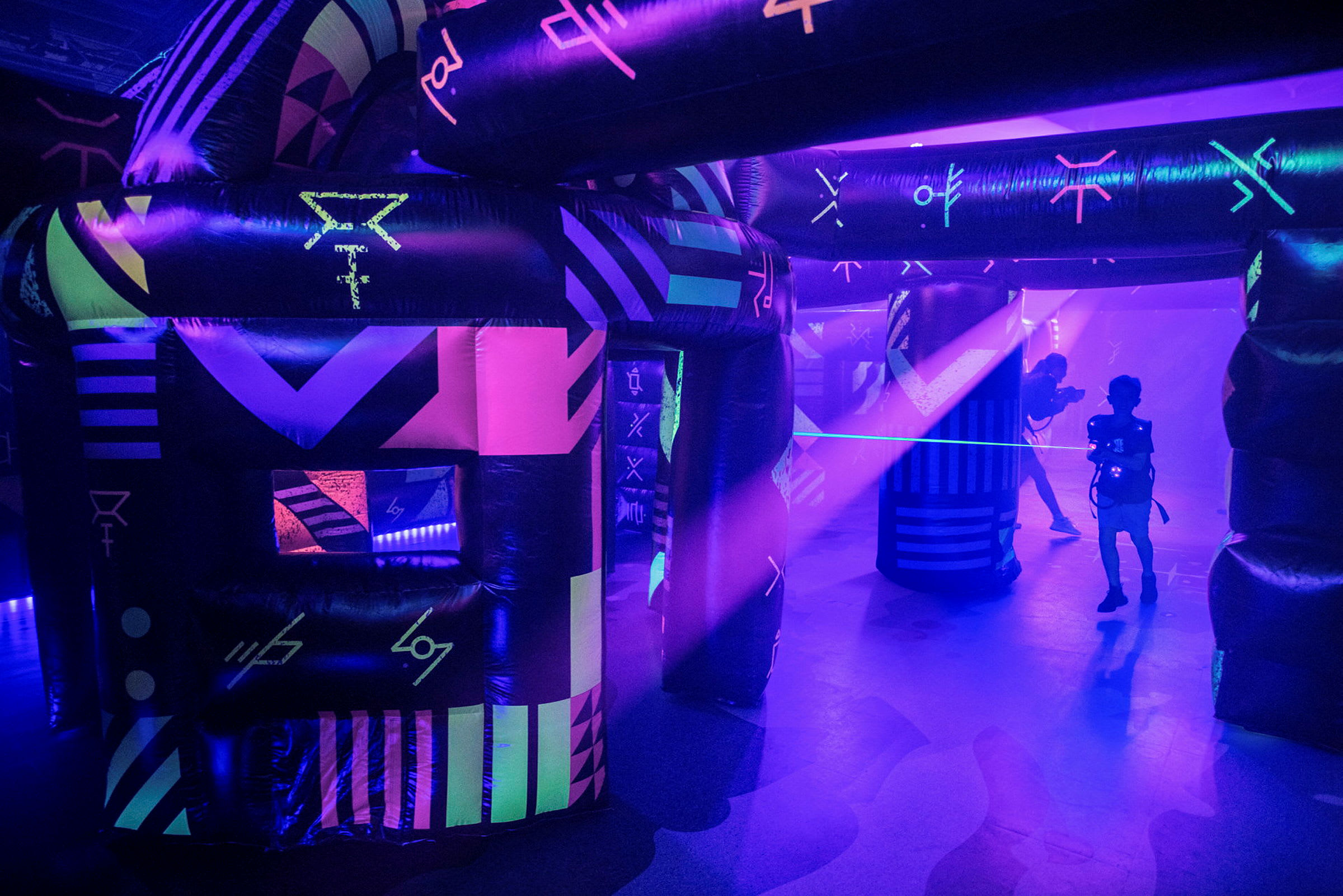 En neonupplyst inomhusmiljö med uppblåsta konstruktioner och personer som spelar laser tag. (AI-genererad text)