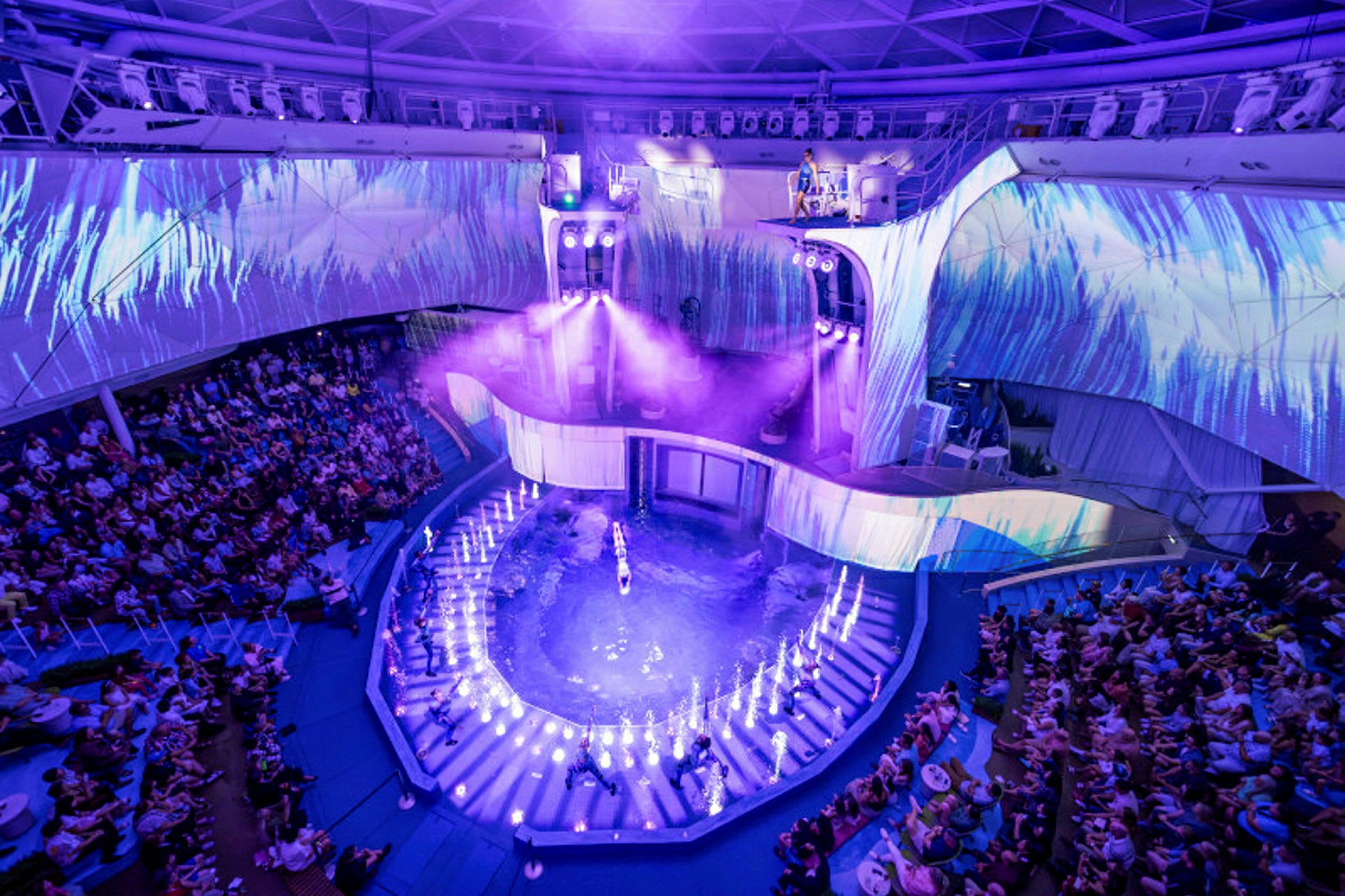 En arena med en vattenföreställning. Publiken sitter runt det upplysta området. (AI-genererad text)
