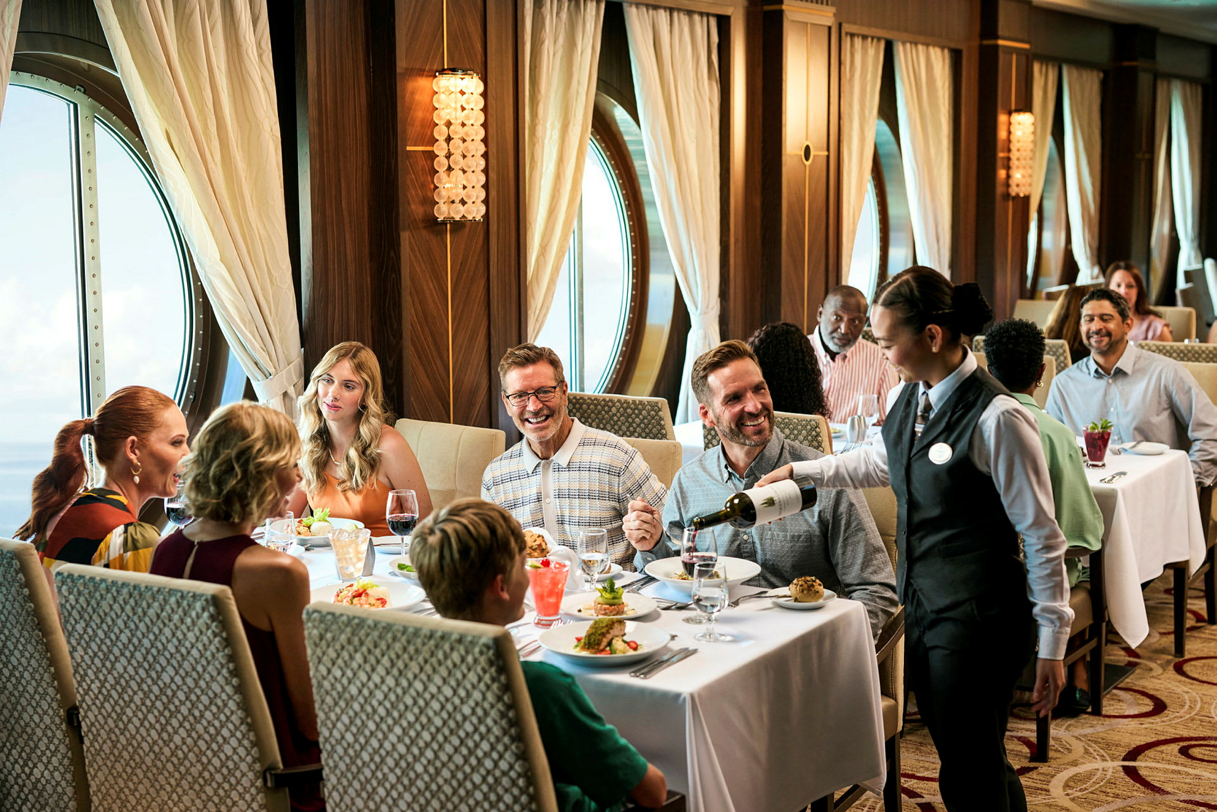 En elegant restaurang med ett fönster med utsikt över havet, där människor njuter av en måltid och en servitör serverar vin. (AI-genererad text)