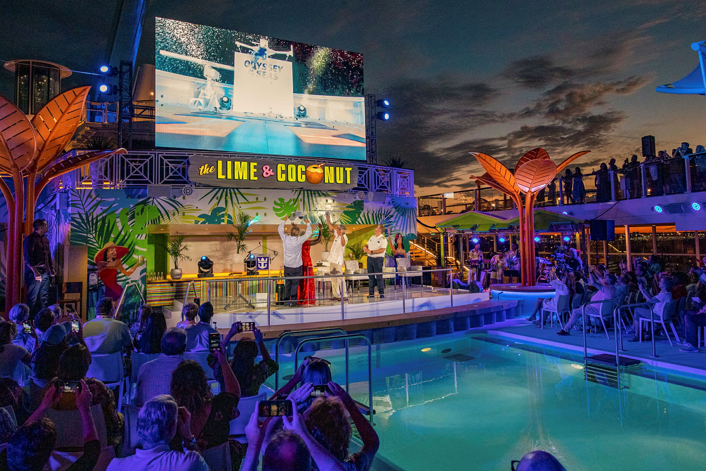 En scen vid en pool med en stor skärm, dekorerad med tropiska motiv och texten "The Lime & Coconut". (AI-genererad text)