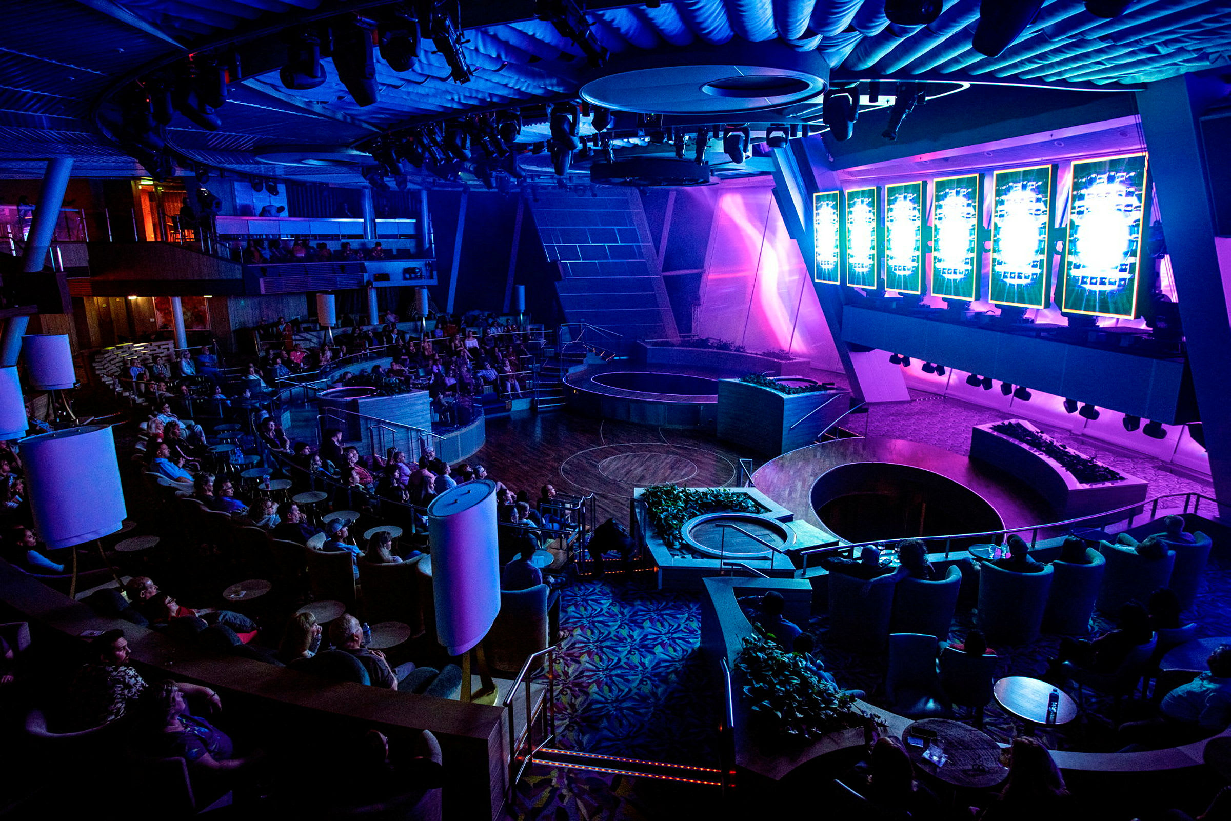 Ett auditorium med lila och blå belysning, försett med sittplatser och en scen. (AI-genererad text)