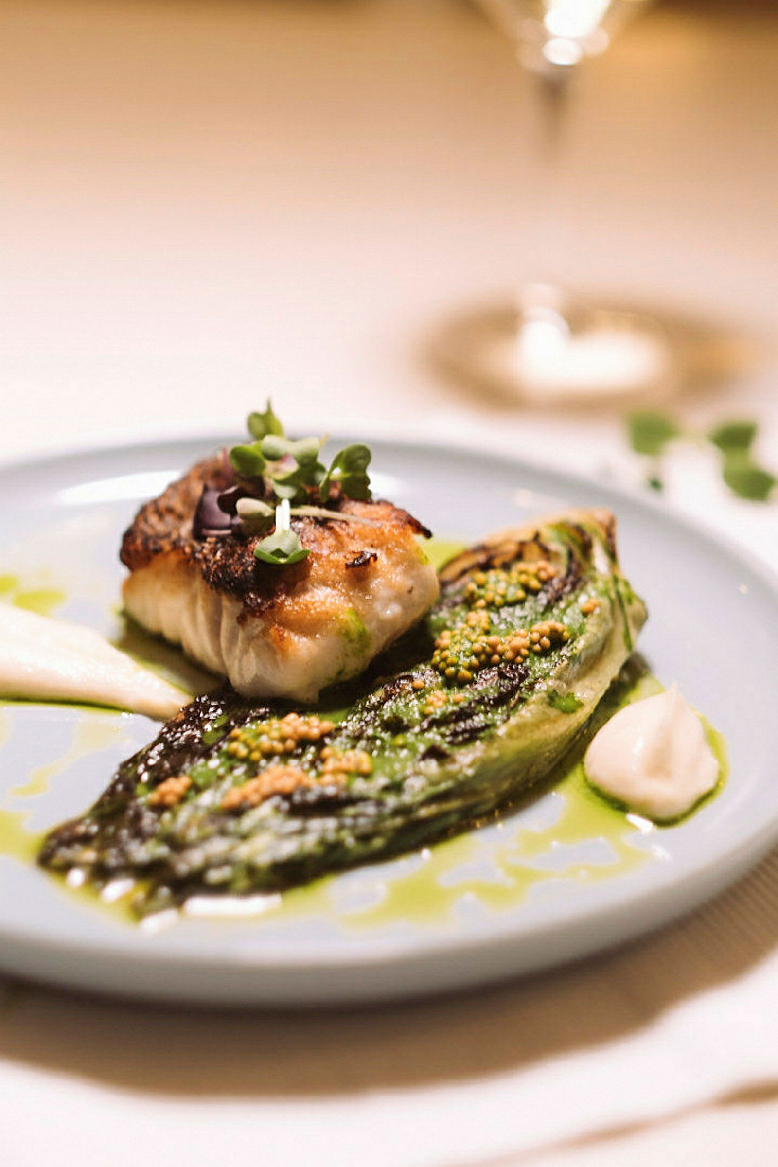 En tallrik med ett tillagat fiskstycke och en grillad salladsklyfta, serverade med sås och färska örter. (AI-genererad text)