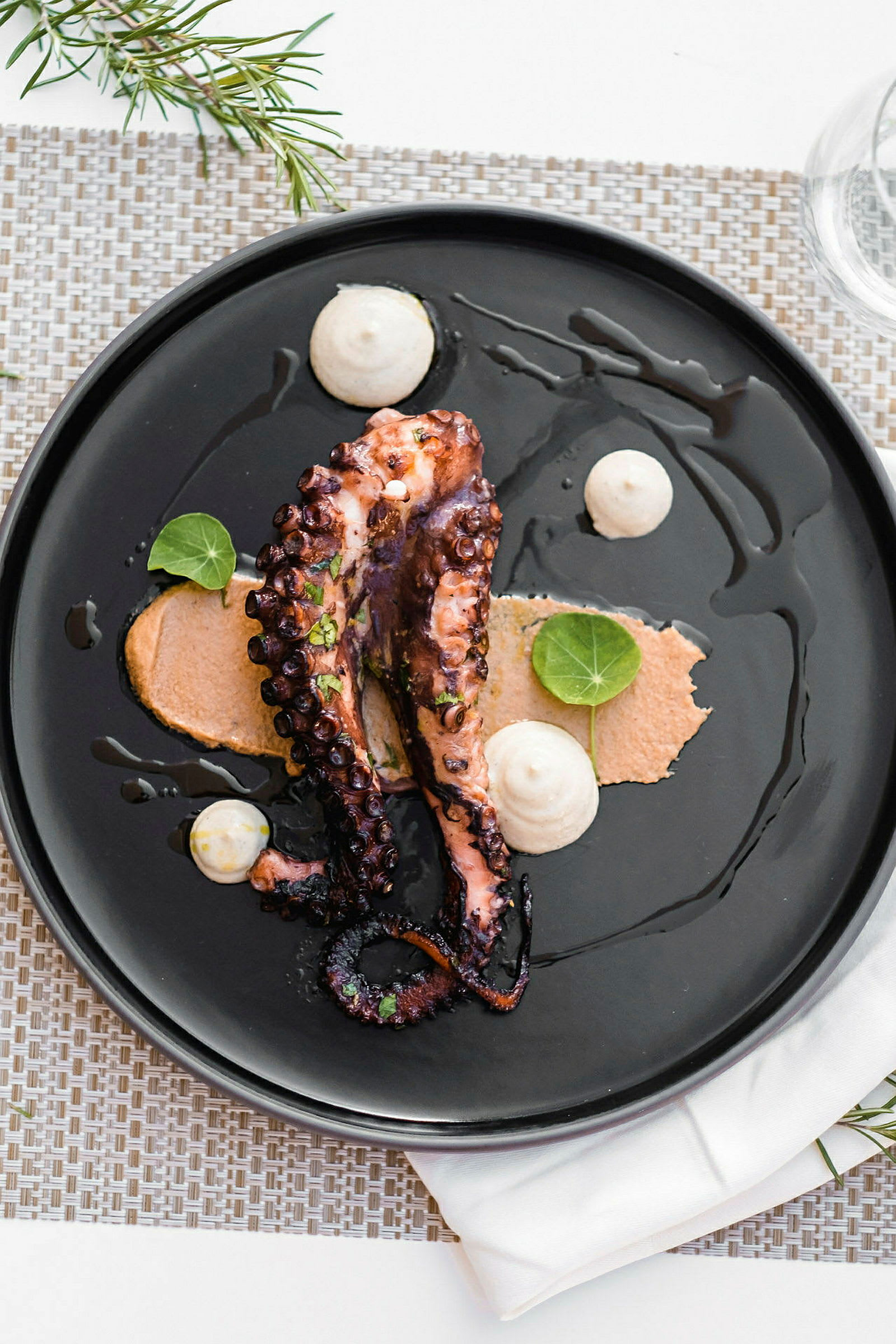 En tallrik med en servering av grillad bläckfisk med sås och dekorativa blad. (AI-genererad text)