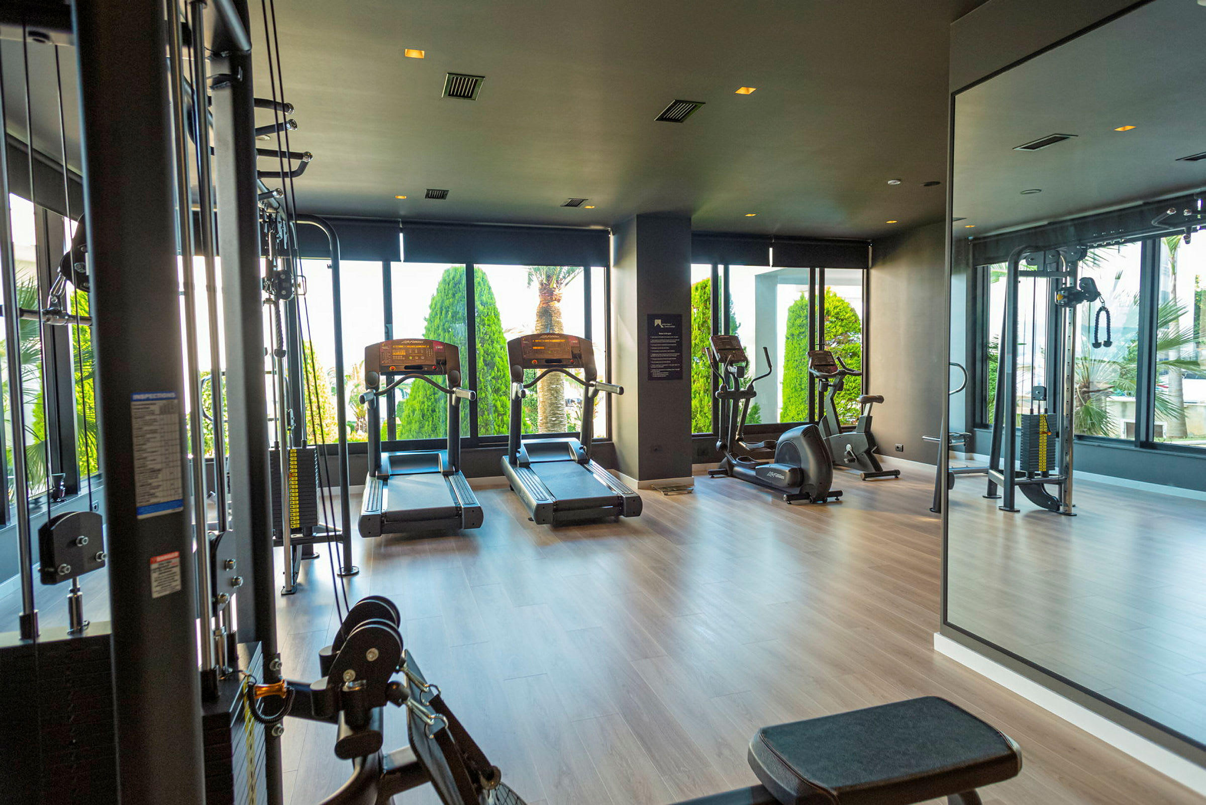 Ett modernt gym med träningsmaskiner och stora fönster. (AI-genererad text)