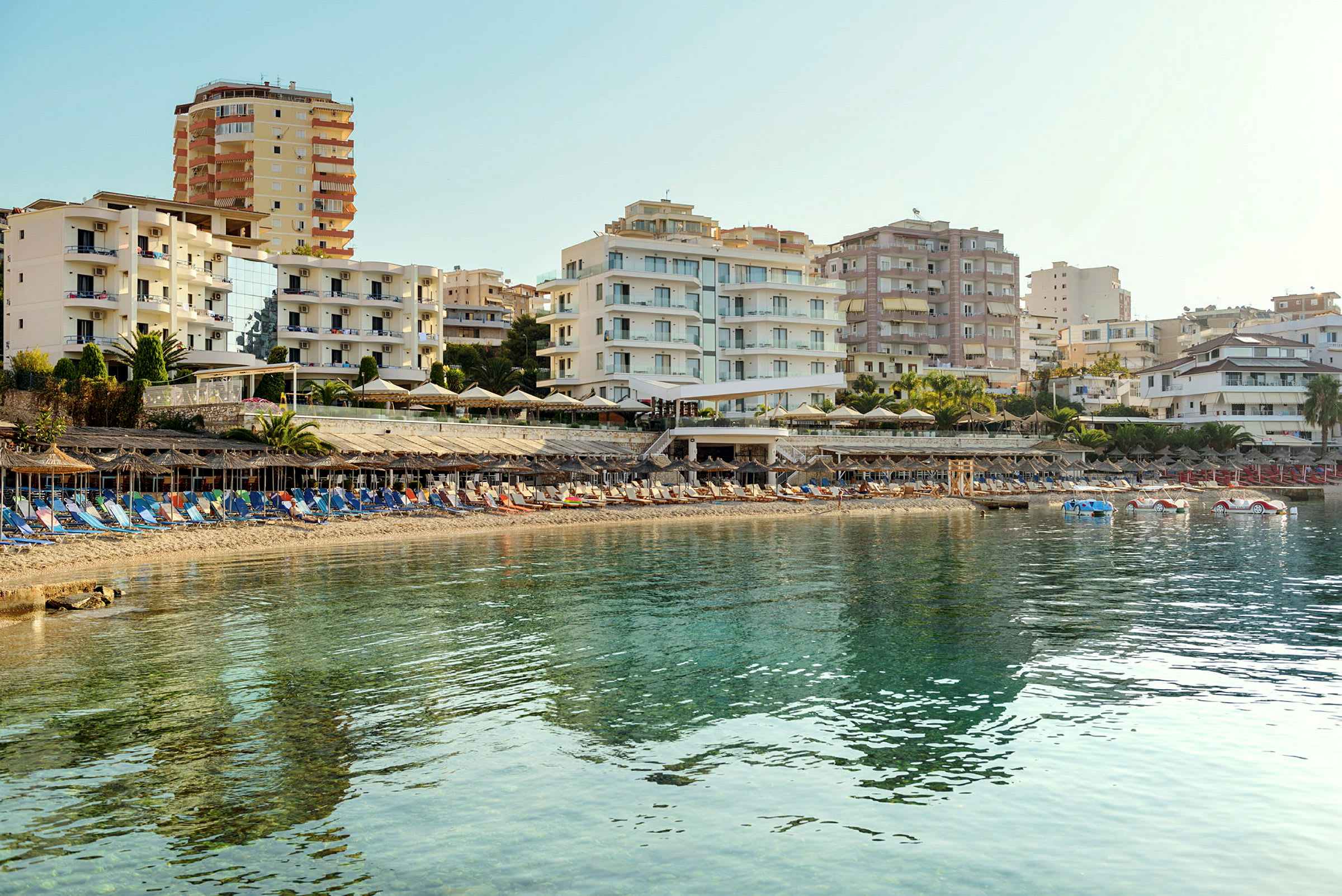 Strand med solstolar och parasoller framför hotellbyggnader. (AI-genererad text)