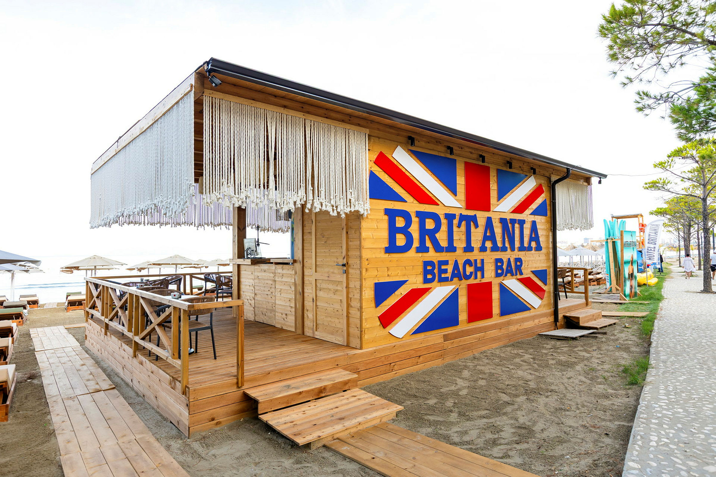 En strandbar med namnet Britania Beach Bar, byggd i trä med utsmyckningar och sittplatser. (AI-genererad text)
