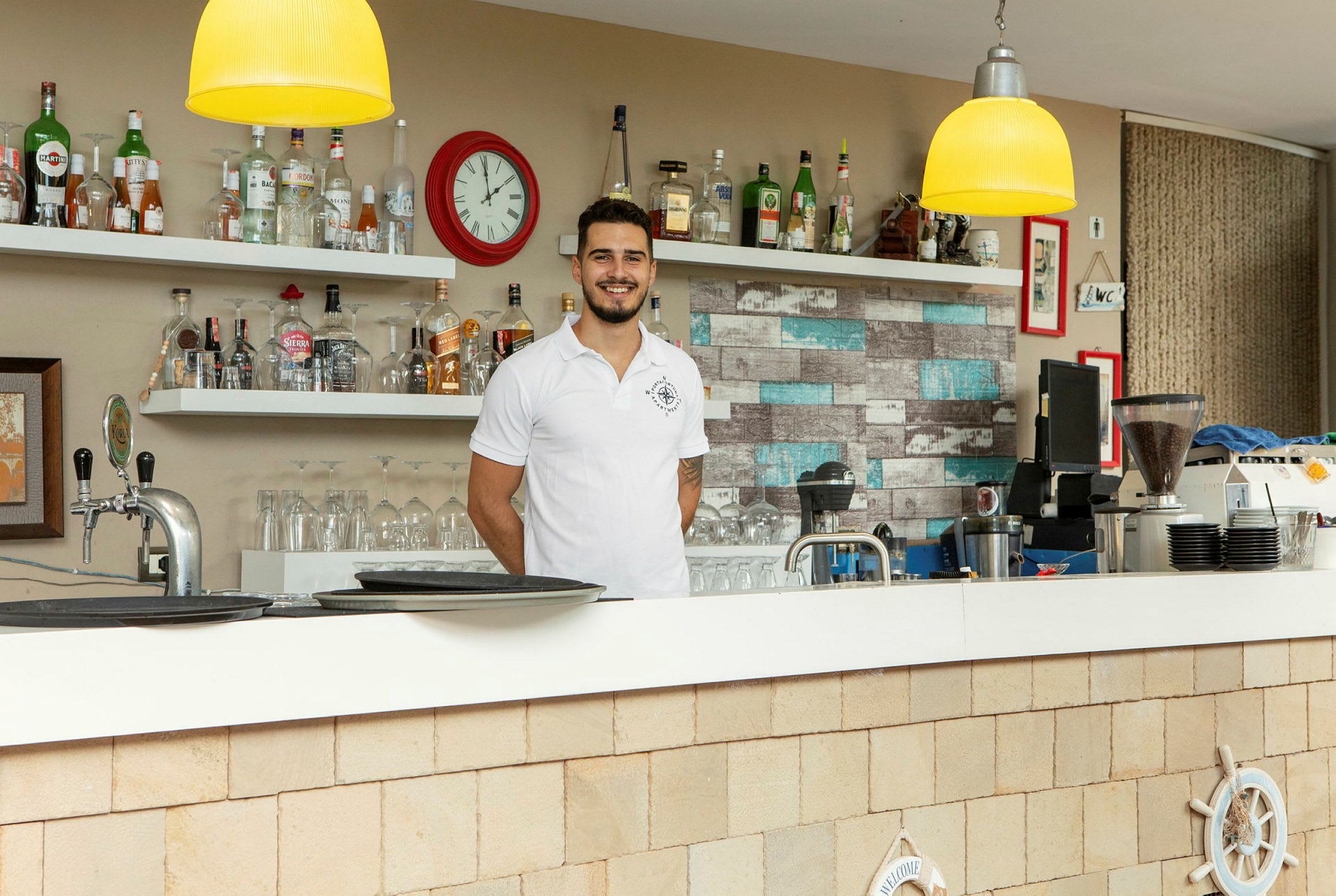 En bar med hyllor fyllda med flaskor och ett klocka på väggen. (AI-genererad text)