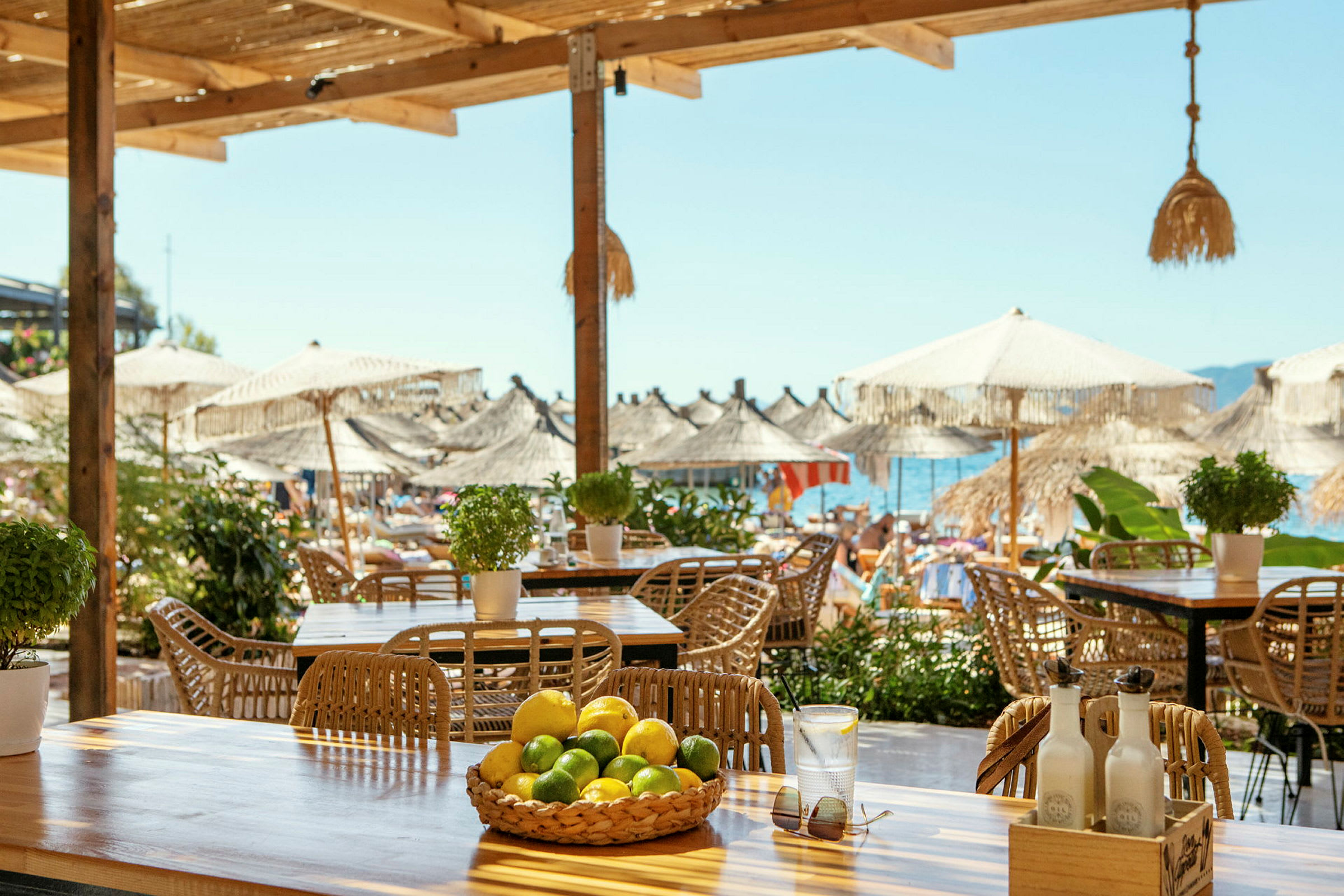 Ett bord med citroner och lime i en korg, med utsikt över en strand med parasoller och havet. (AI-genererad text)
