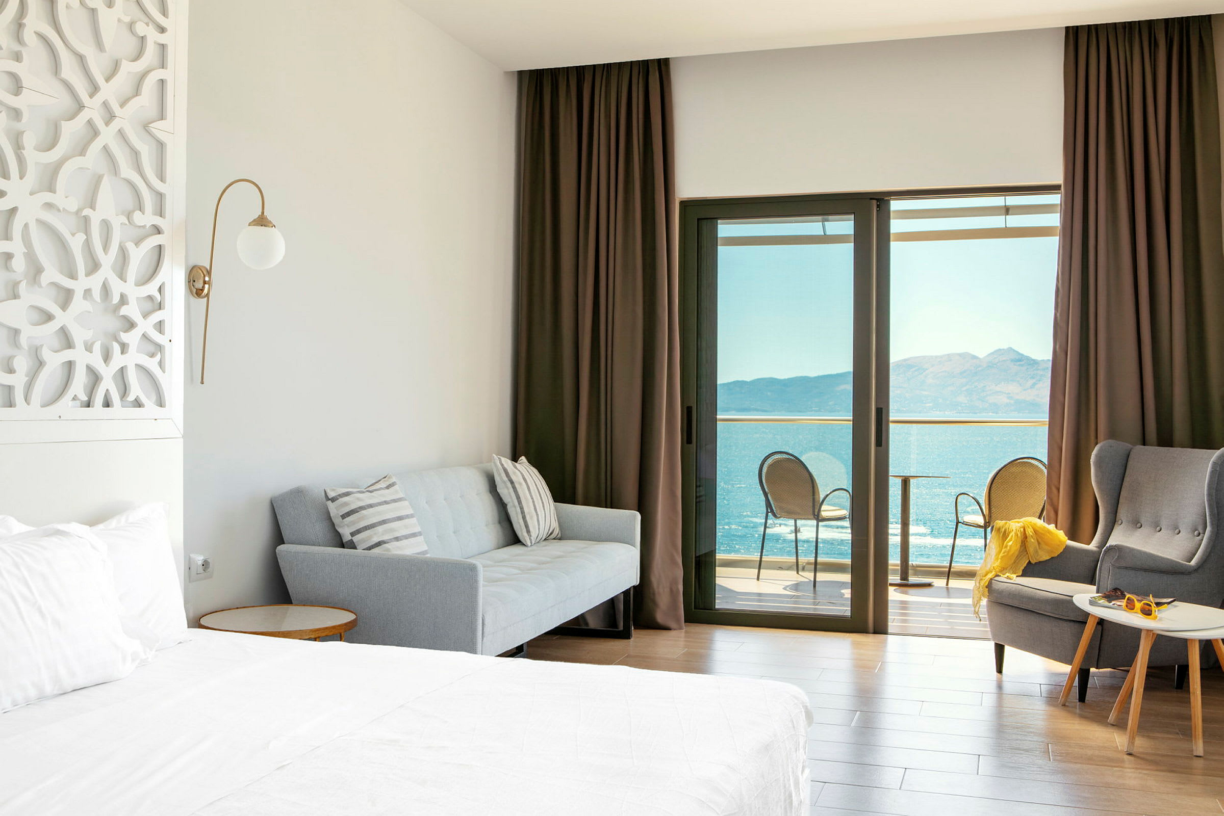 Hotellrum med säng, soffa, fåtölj och balkong med havsutsikt. (AI-genererad text)