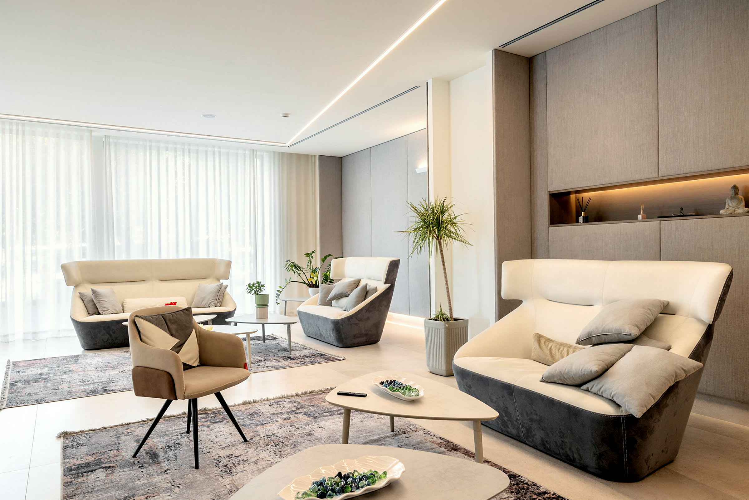 En modern lounge med ljus inredning, flera bekväma fotöljer och soffor, växter och dekorativa föremål. (AI-genererad text)