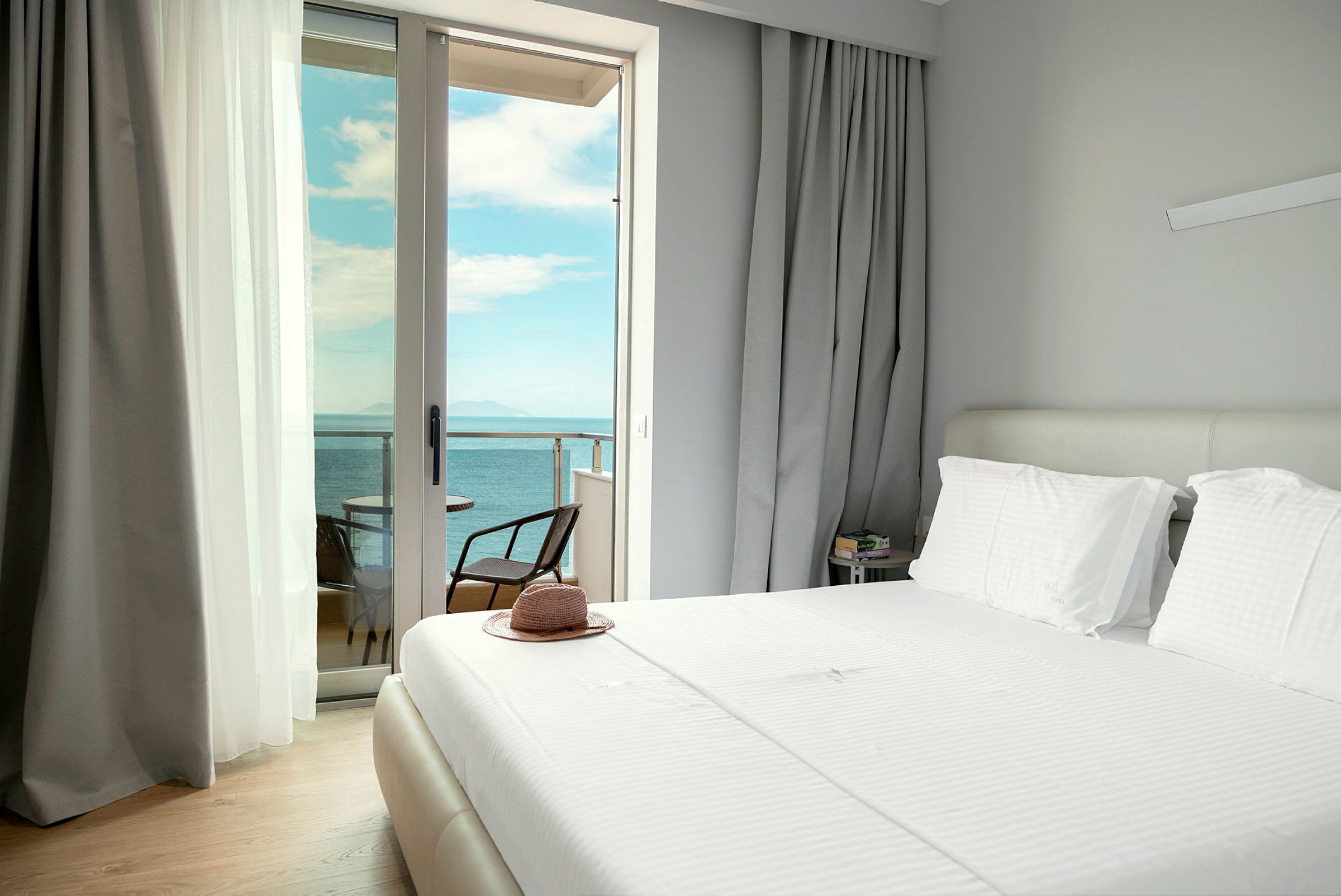 Ett hotellrum med en bäddad säng och öppna gardiner som visar en utsikt över havet från balkongen. (AI-genererad text)