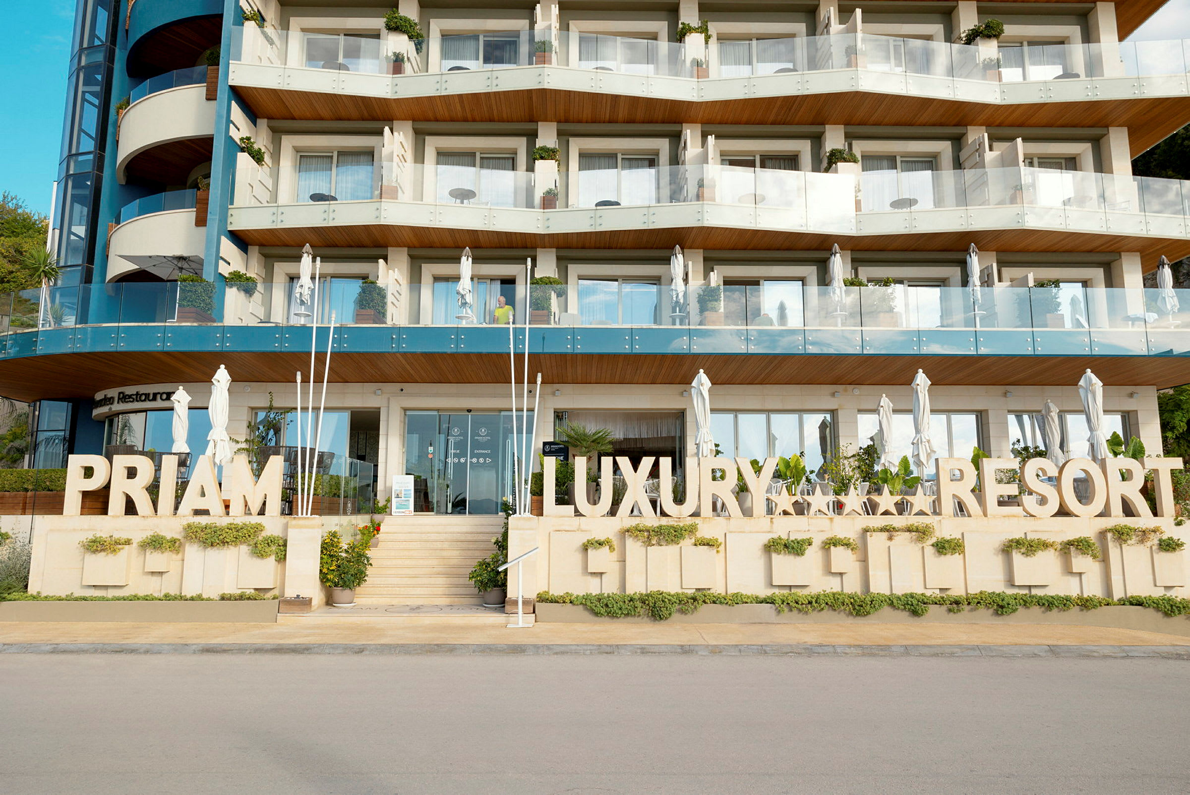 Flera våningar av ett hotell byggt i modern arkitektur med en tydlig skylt som säger 'Priam Luxury Resort'. (AI-genererad text)