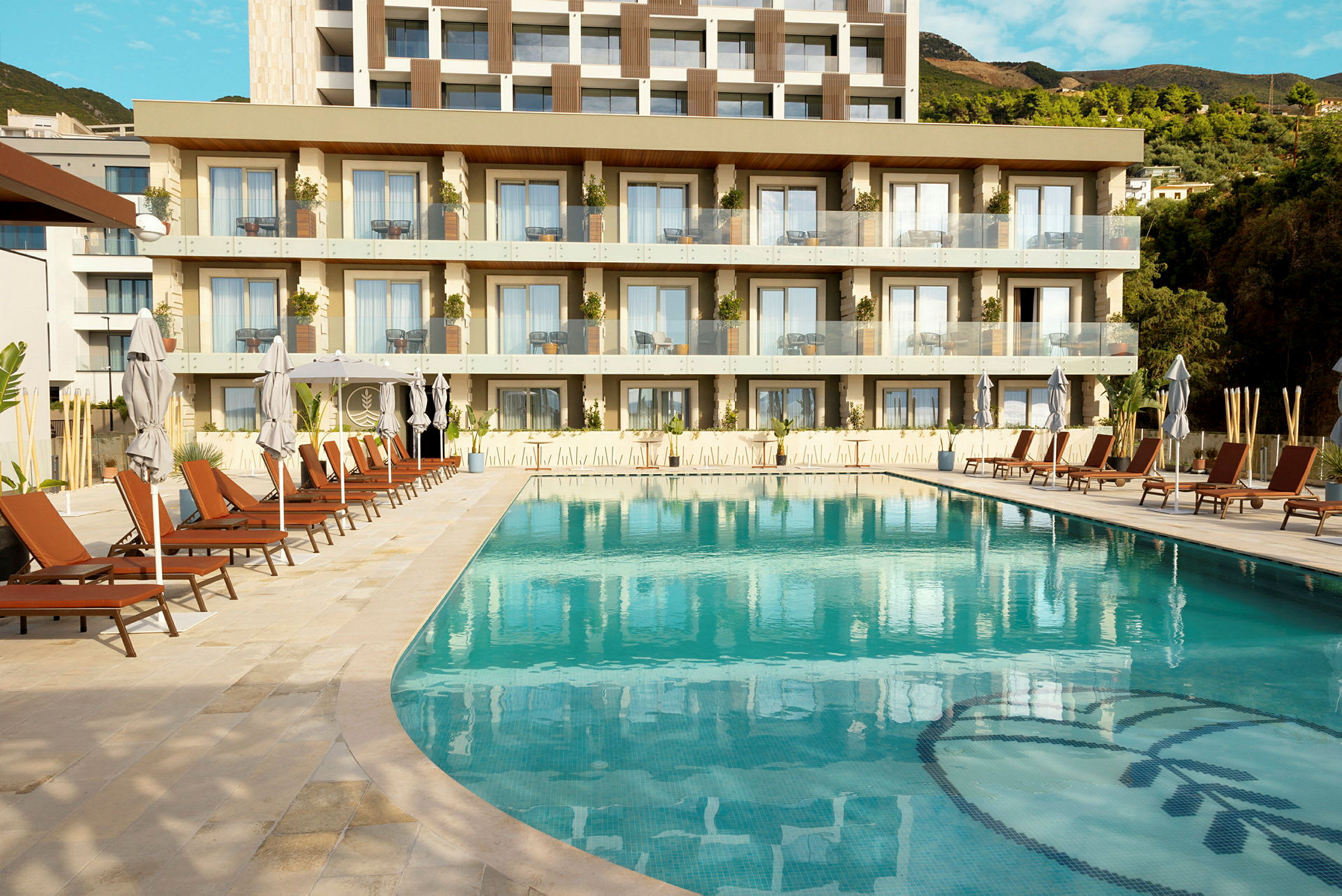 Bild av en pool med solstolar och parasoller framför ett modernt hotell med balkonger. (AI-genererad text)